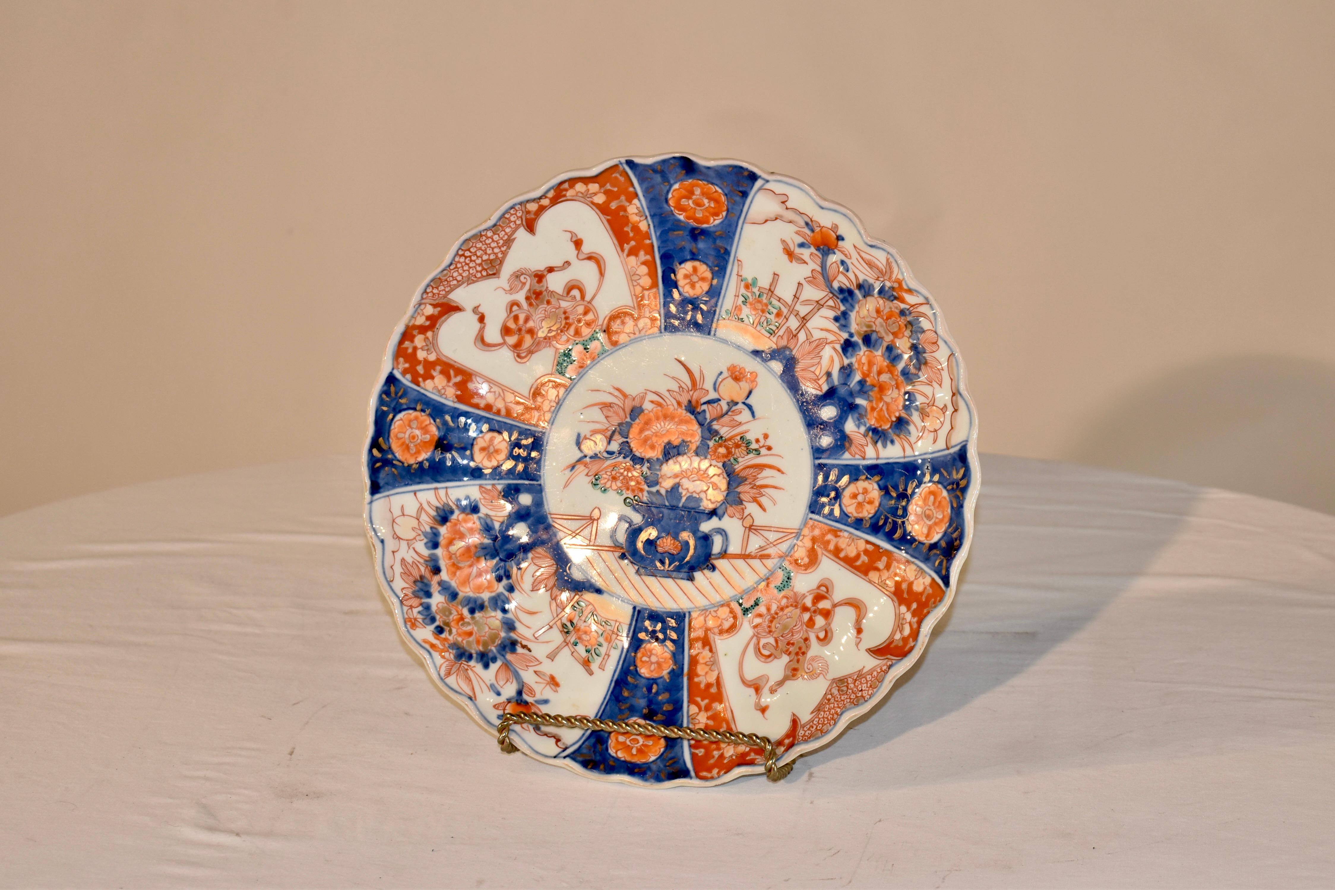 Late 19th century Imari plate. This is a lovely deep plate with scalloped edges. The central medallion has hand painted florals in a jardiniere, surrounded by four hand painted cobalt stripes, decorated with florals and separated by wider panels of