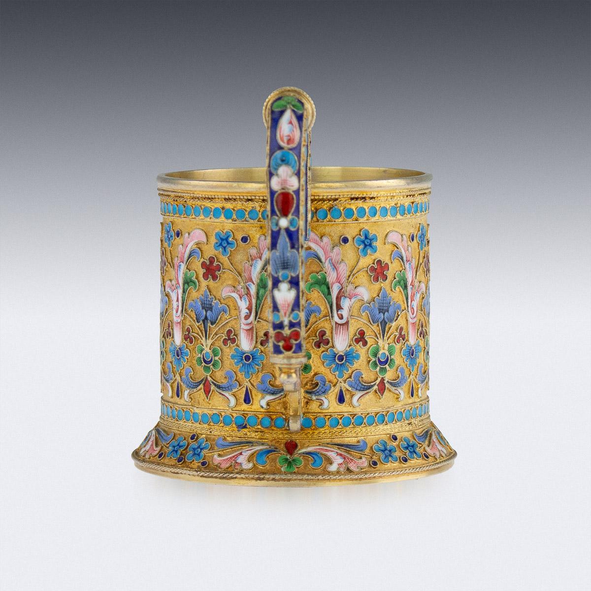 Antique 19th century imperial Russian solid silver-gilt and cloisonné enamel tea glass holder, circular with upswept key-formed handle, plain rim and spreading domed foot, body profusely decorated with floral motifs in vary-colored cloisonné enamel