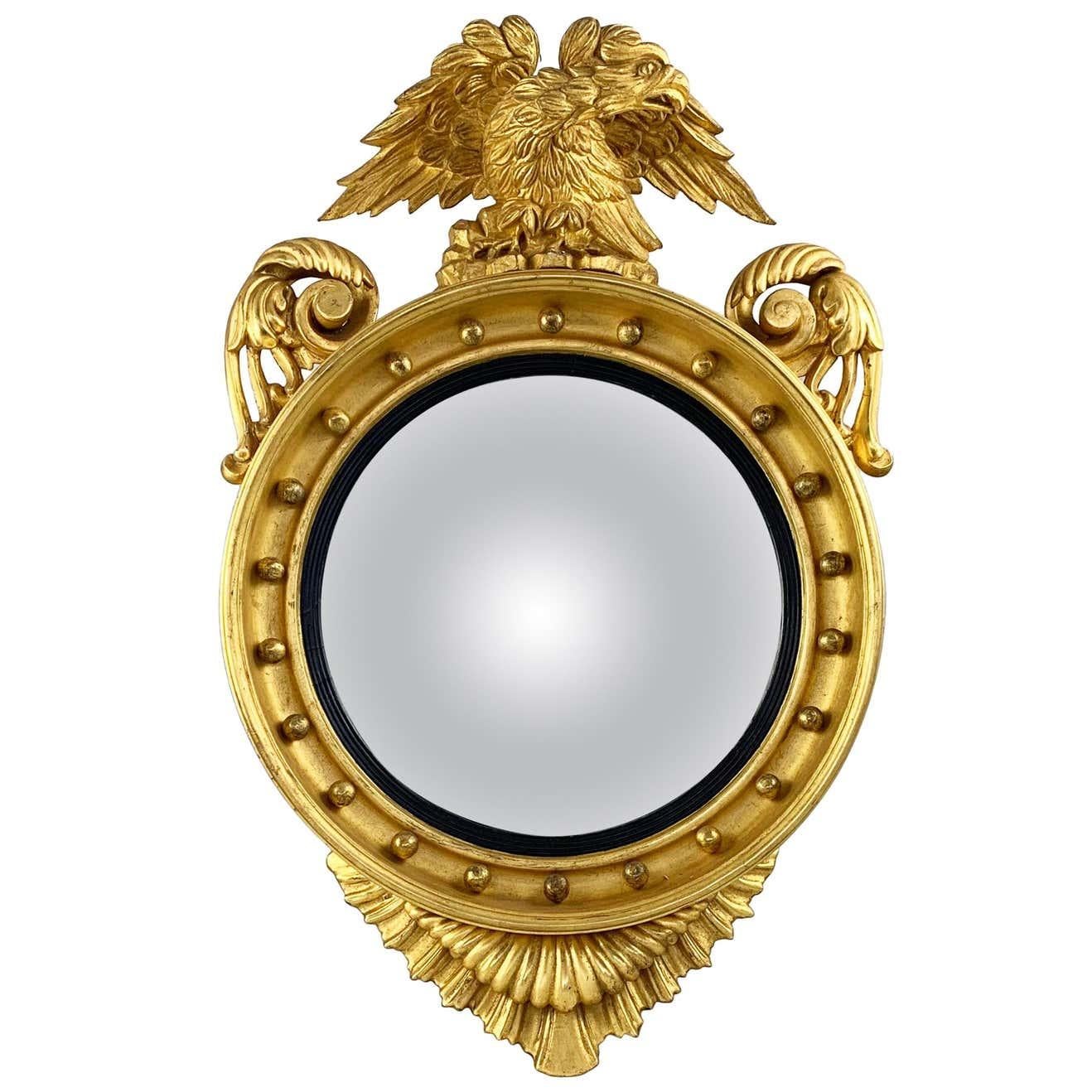 An impressive Regency giltwood carved convex wall mirror. 19th century. With ebonized rim and surmounted by an Eagle.