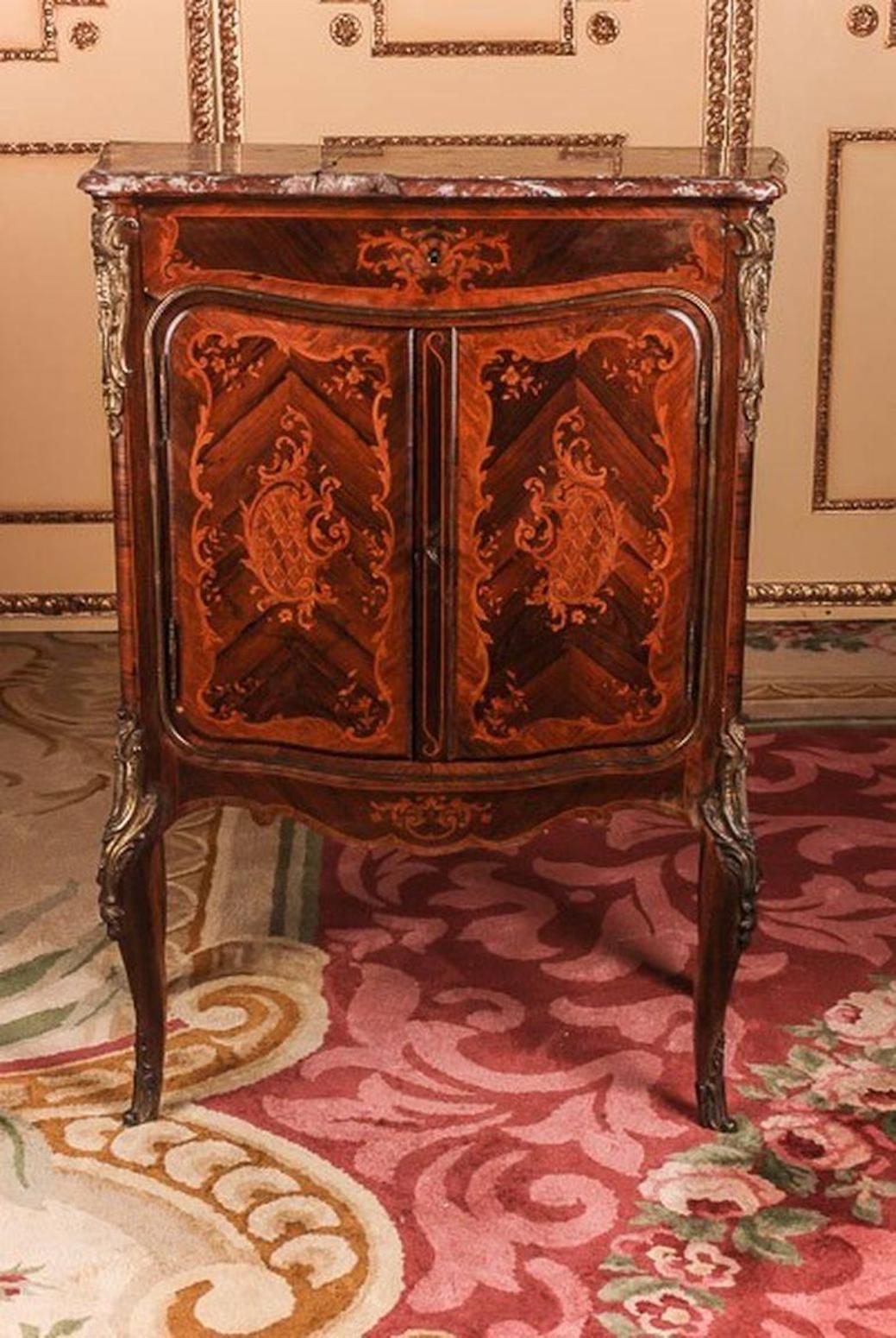 Impiallacciatura Bois-Satiné, rivestimento integrale a specchio e intarsio su conifere massicce. Con finiture in bronzo dorato a fuoco, finemente cesellato e altamente decorativo, con rocaille traforata. Corpo singolare a due gambe su gambe oblique