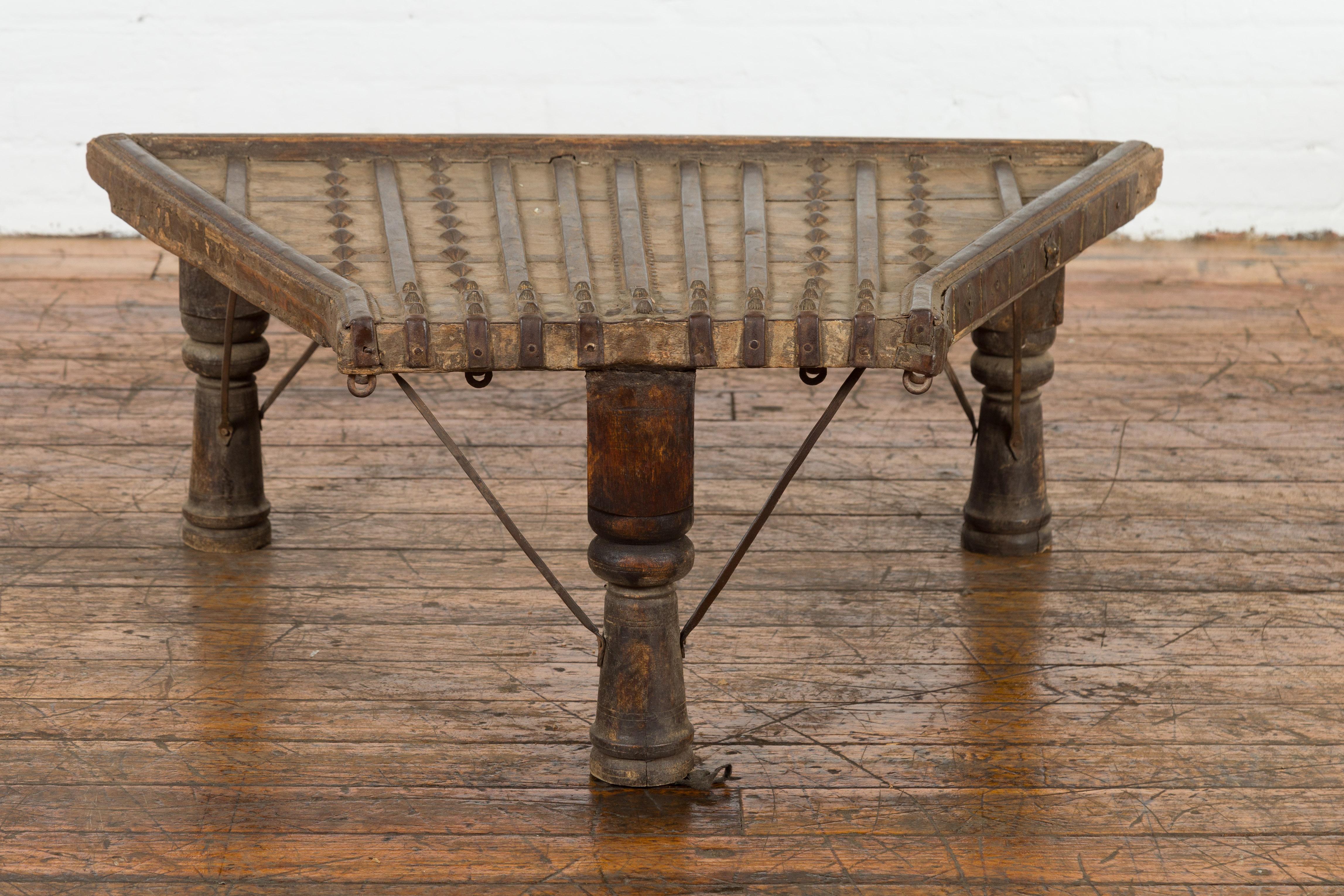 An antique rustic Indian handmade coffee table from the 19th century with trapezoidal top, iron stretchers, turned baluster legs and weathered patina. Created in India during the 19th century, this piece is made of the front portion of a bullock
