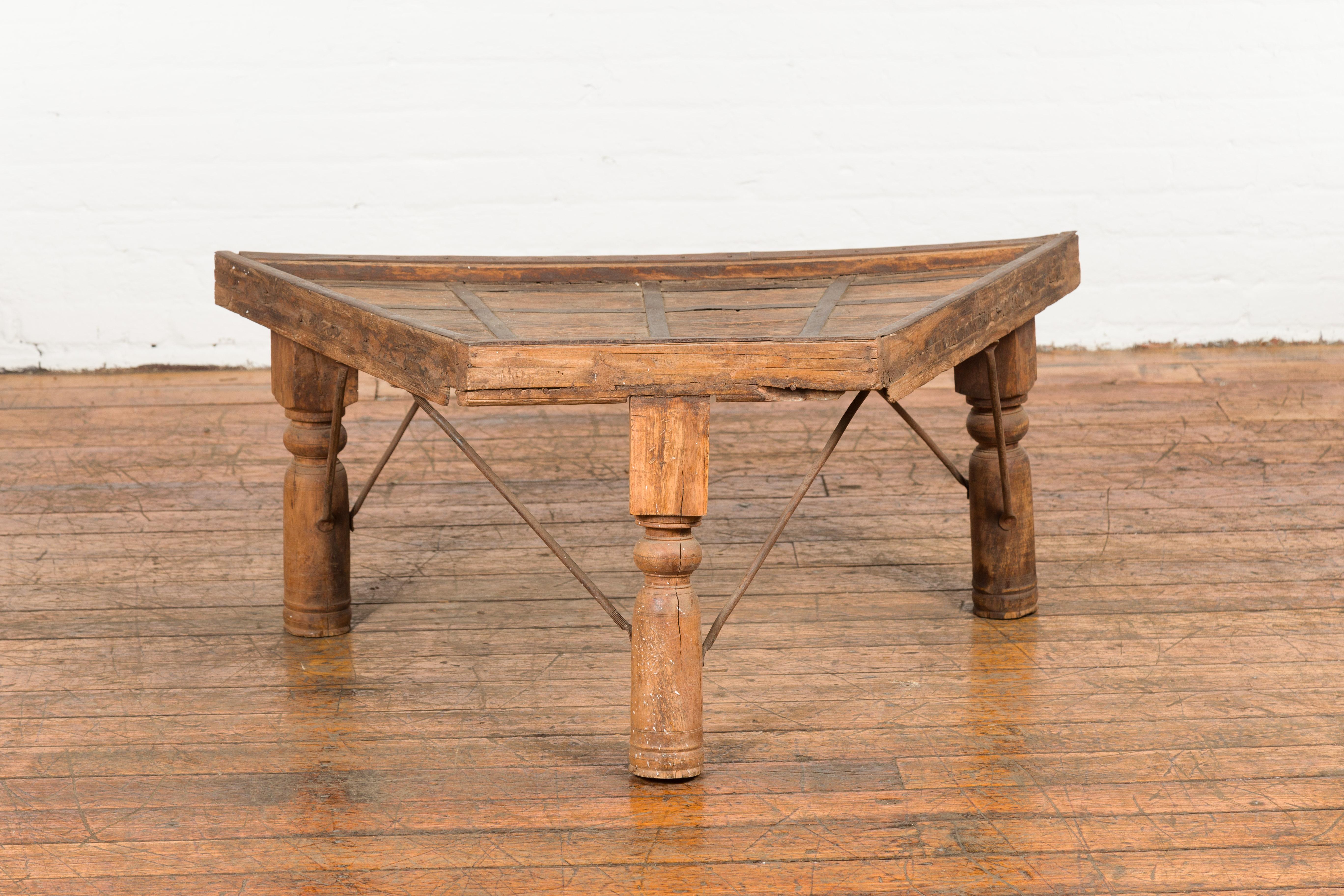 An antique rustic Indian handmade coffee table from the 19th century with trapezoidal top, iron stretchers, turned baluster legs and weathered patina. Created in India during the 19th century, this piece is made of the front portion of a bullock