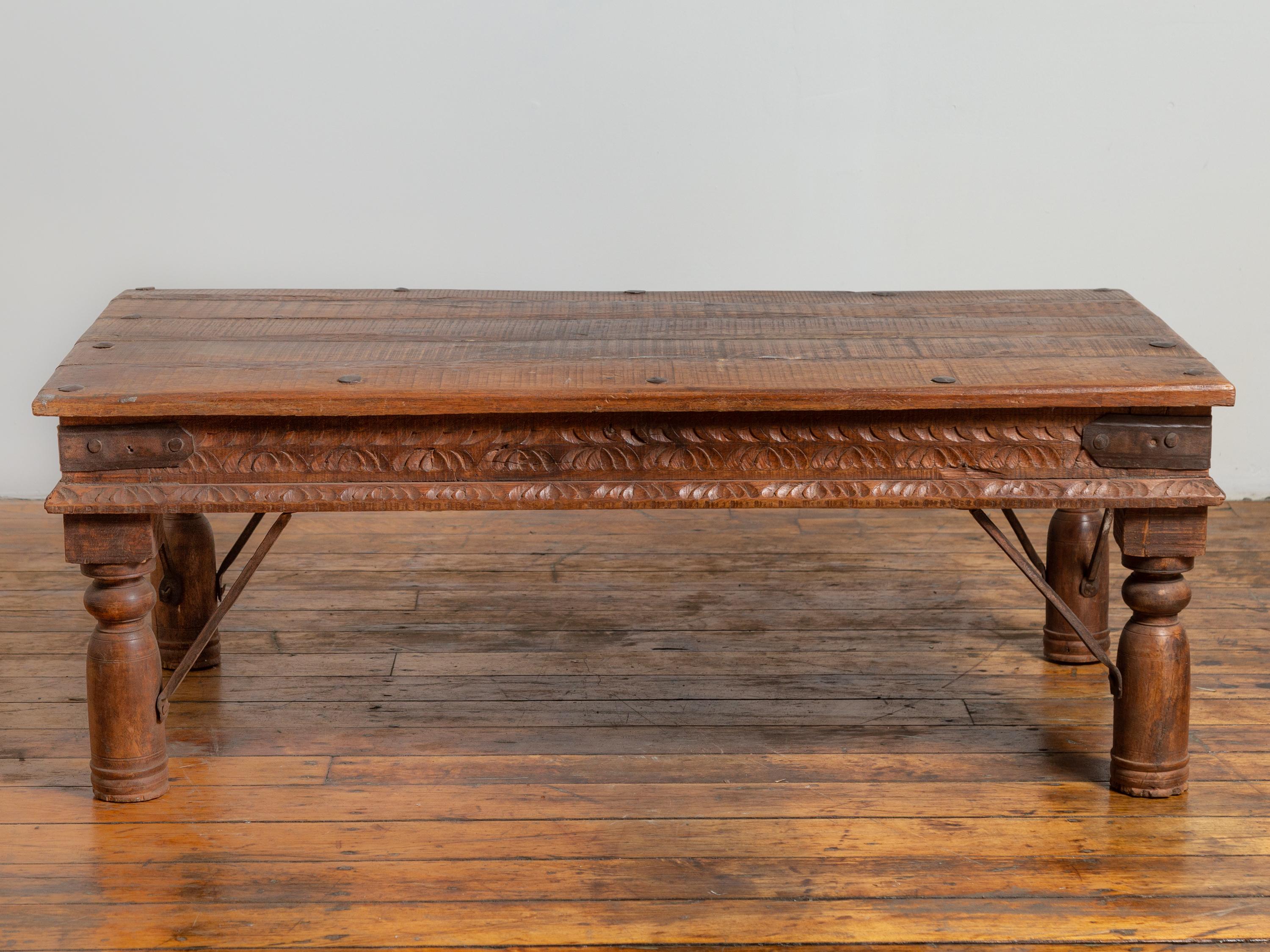 An antique rustic Indian low coffee table from the 19th century, with iron accents and baluster legs. Born in India during the 19th century this charming coffee table features a rectangular planked top with iron nailheads, sitting above an elegant