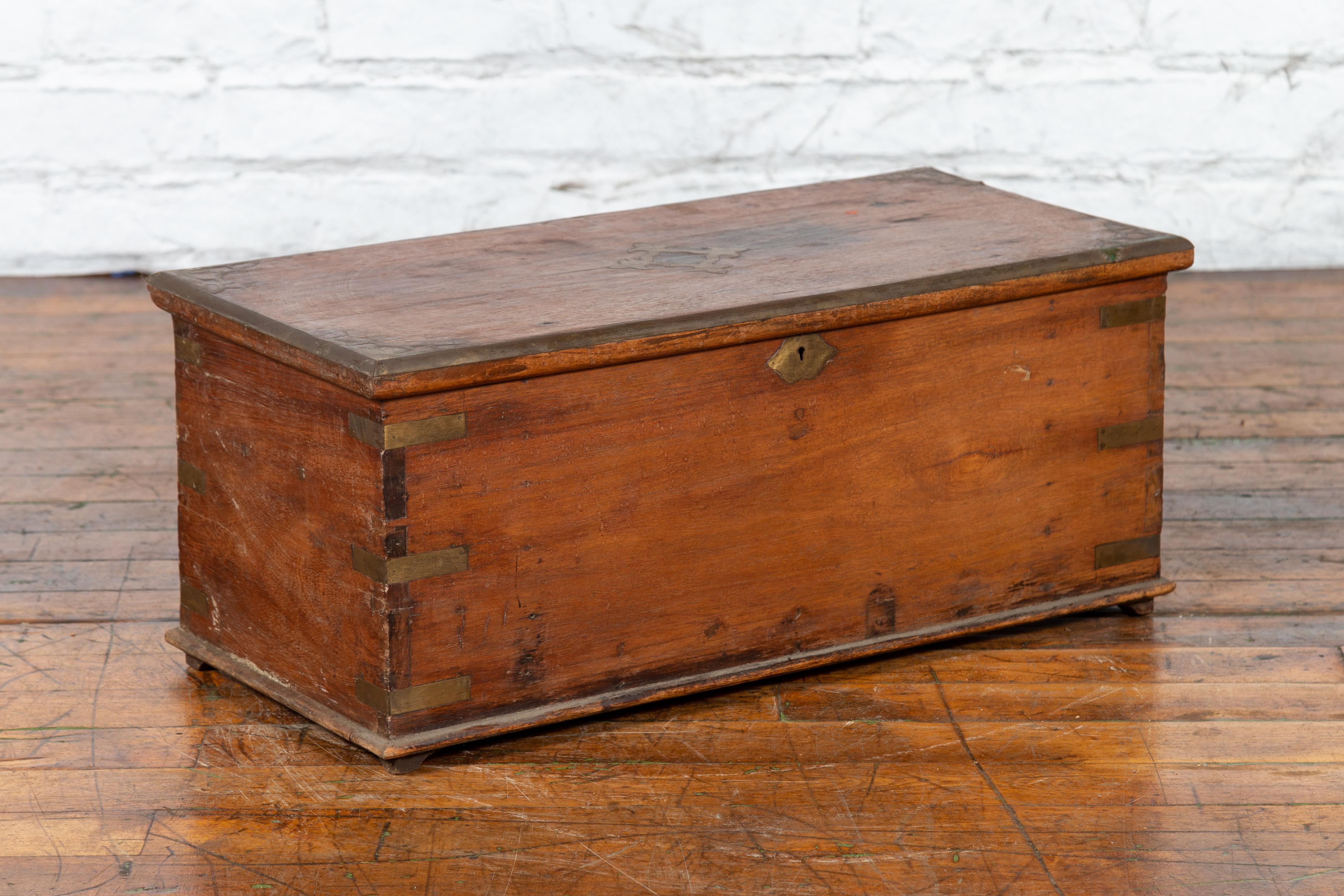 An antique Indian wooden trunk from the 19th century, with brass inlay and bracket feet. Created in India during the 19th century, this wooden trunk features a rectangular lid adorned with an ornate brass inlay, opening to reveal an organized