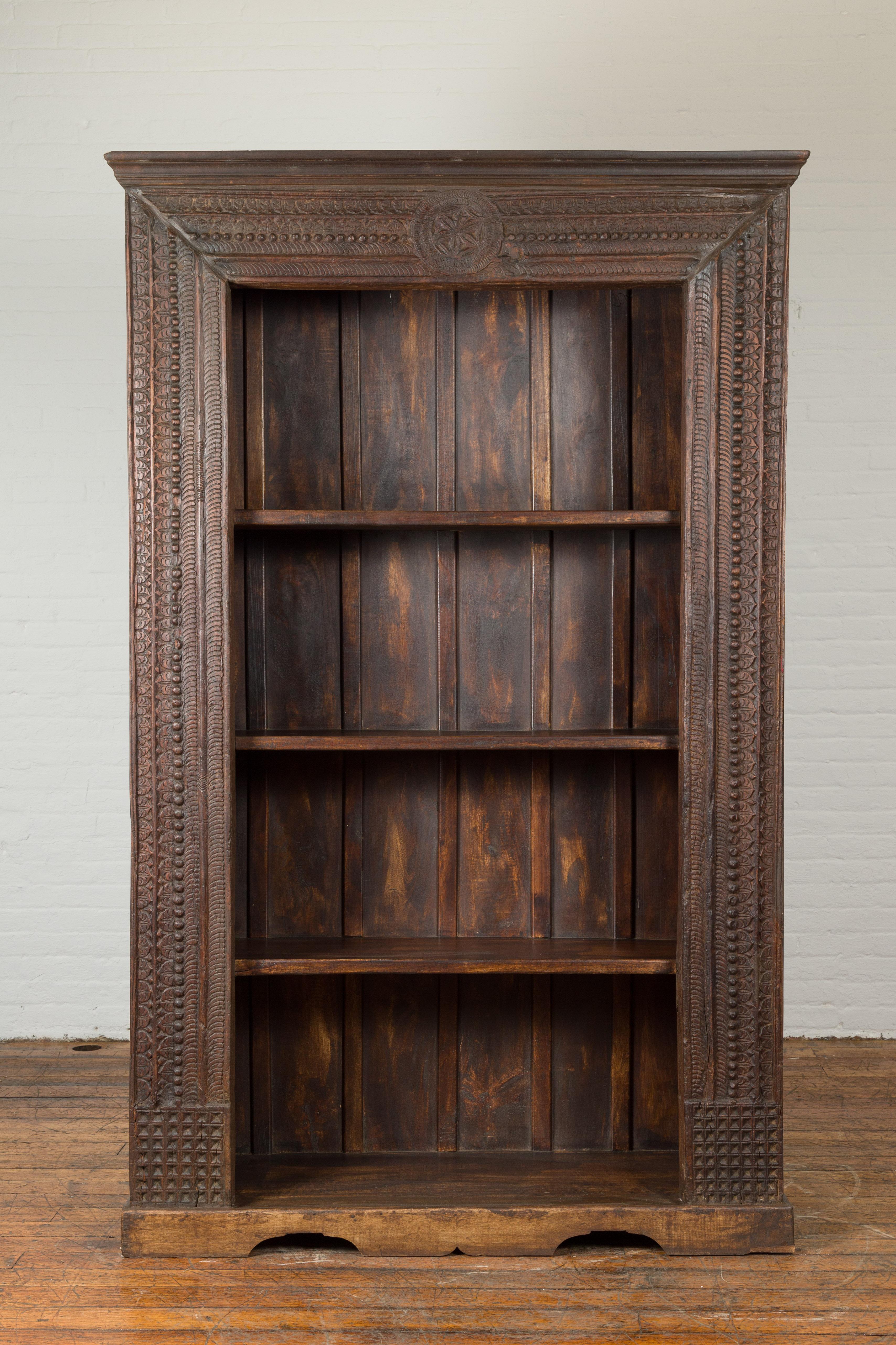 An Indian Gujarat wooden bookcase from the 19th century, with carved rosette and foliage. Created on the Western coast of India during the 19th century, this wooden bookcase features a linear silhouette accented with an abundance of carved friezes