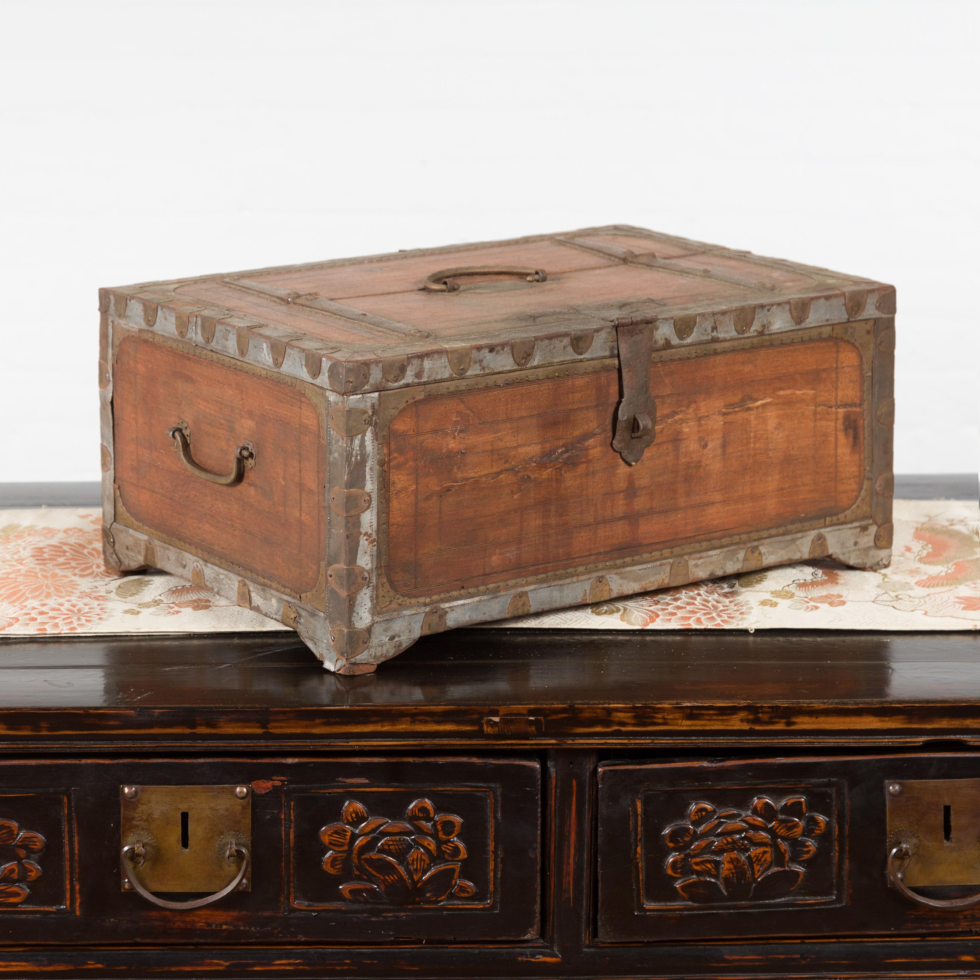 An antique Indian wooden box from the 19th century, with brass details and weathered appearance. Topped with a rectangular lid fitted with a c-scroll handle and half opening to reveal a small distressed interior with side partitioned compartment,