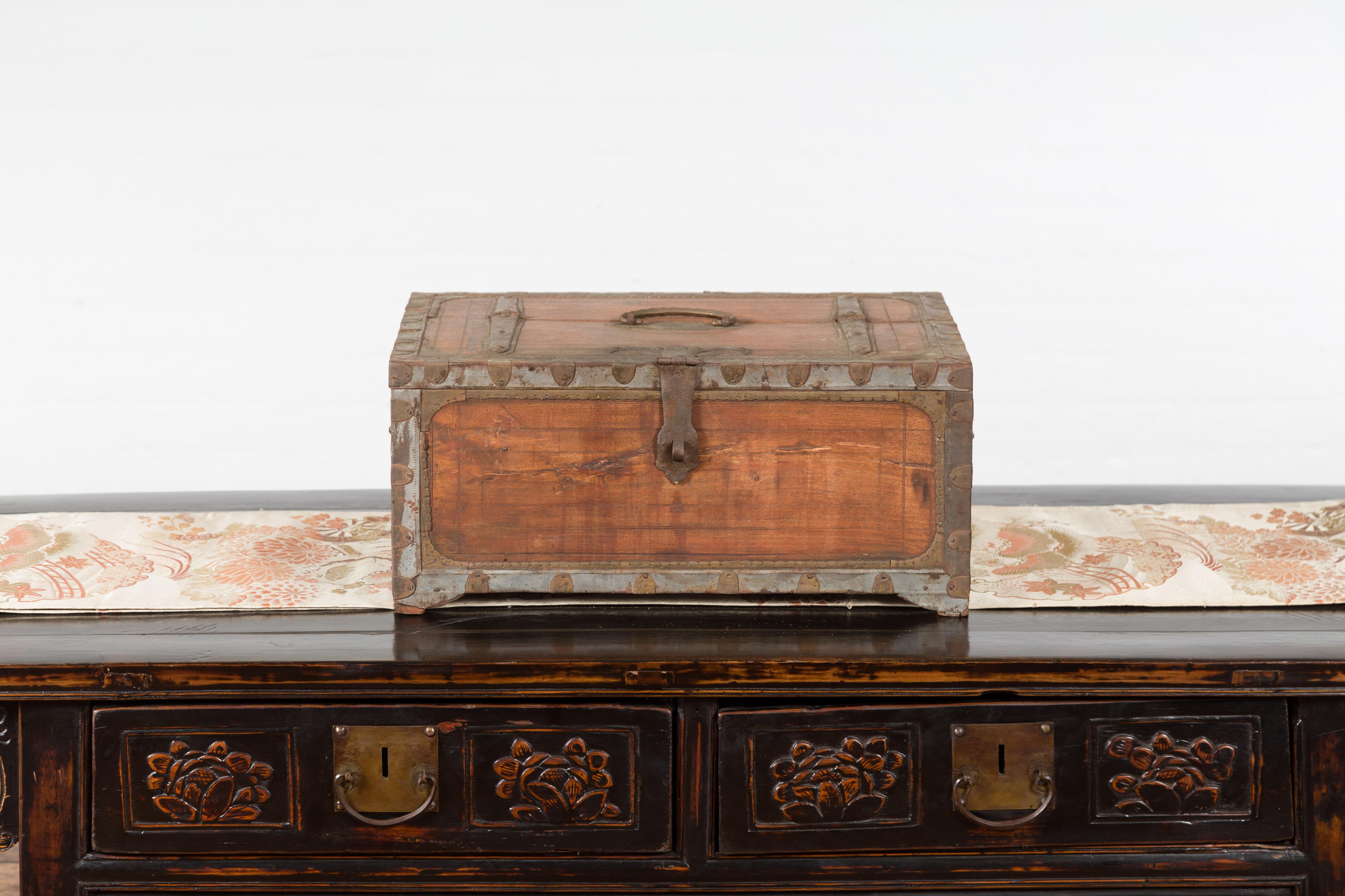 An antique Indian wooden box from the 19th century, with brass details and weathered appearance. Topped with a rectangular lid fitted with a c-scroll handle and half opening to reveal a small distressed interior with side partitioned compartment,