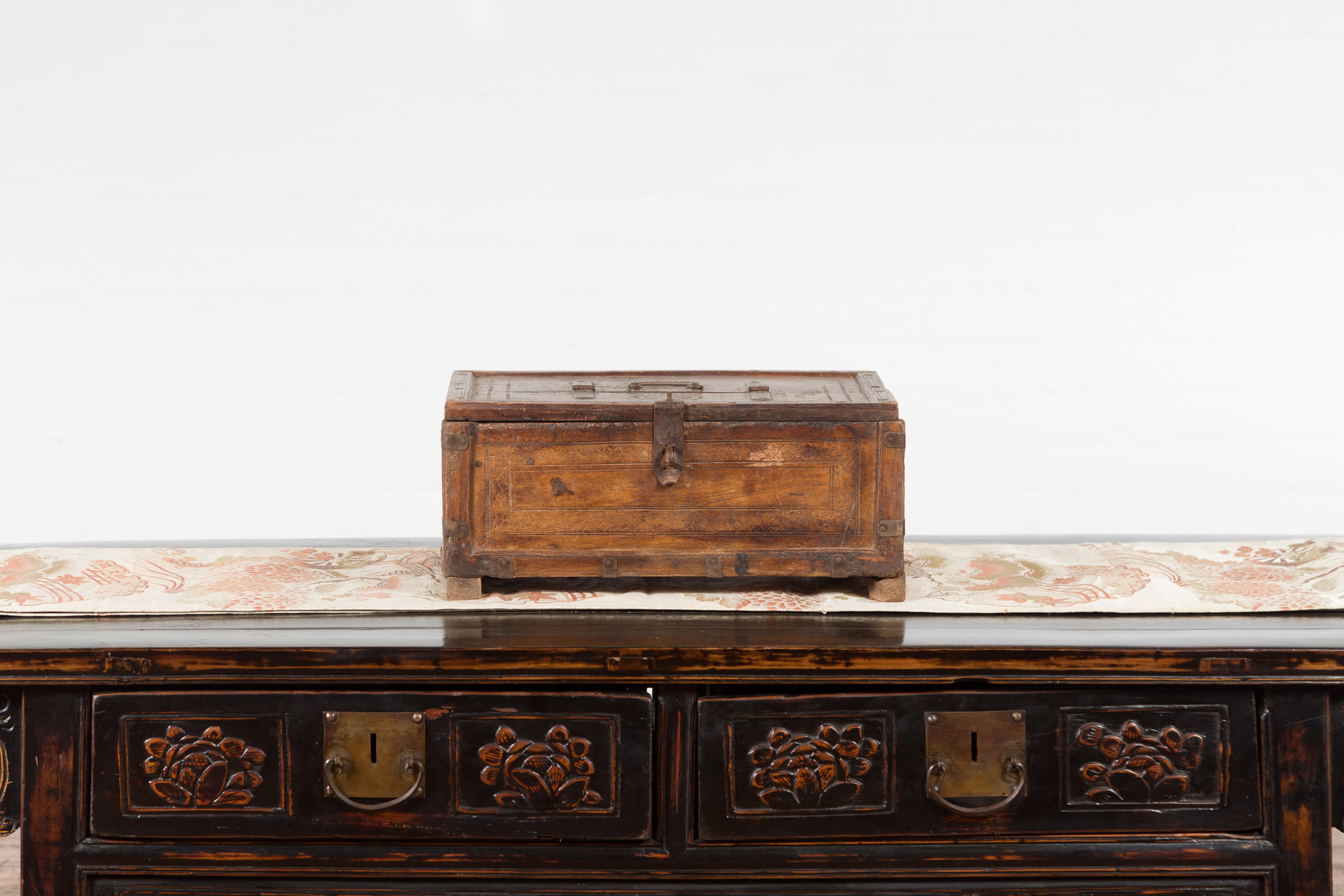 An Indian antique wooden box from the 19th century, with incised motifs and distressed patina. Topped with a rectangular lid accented with pierced concentric circles and half opening to reveal a small interior, this old Indian box is adorned with