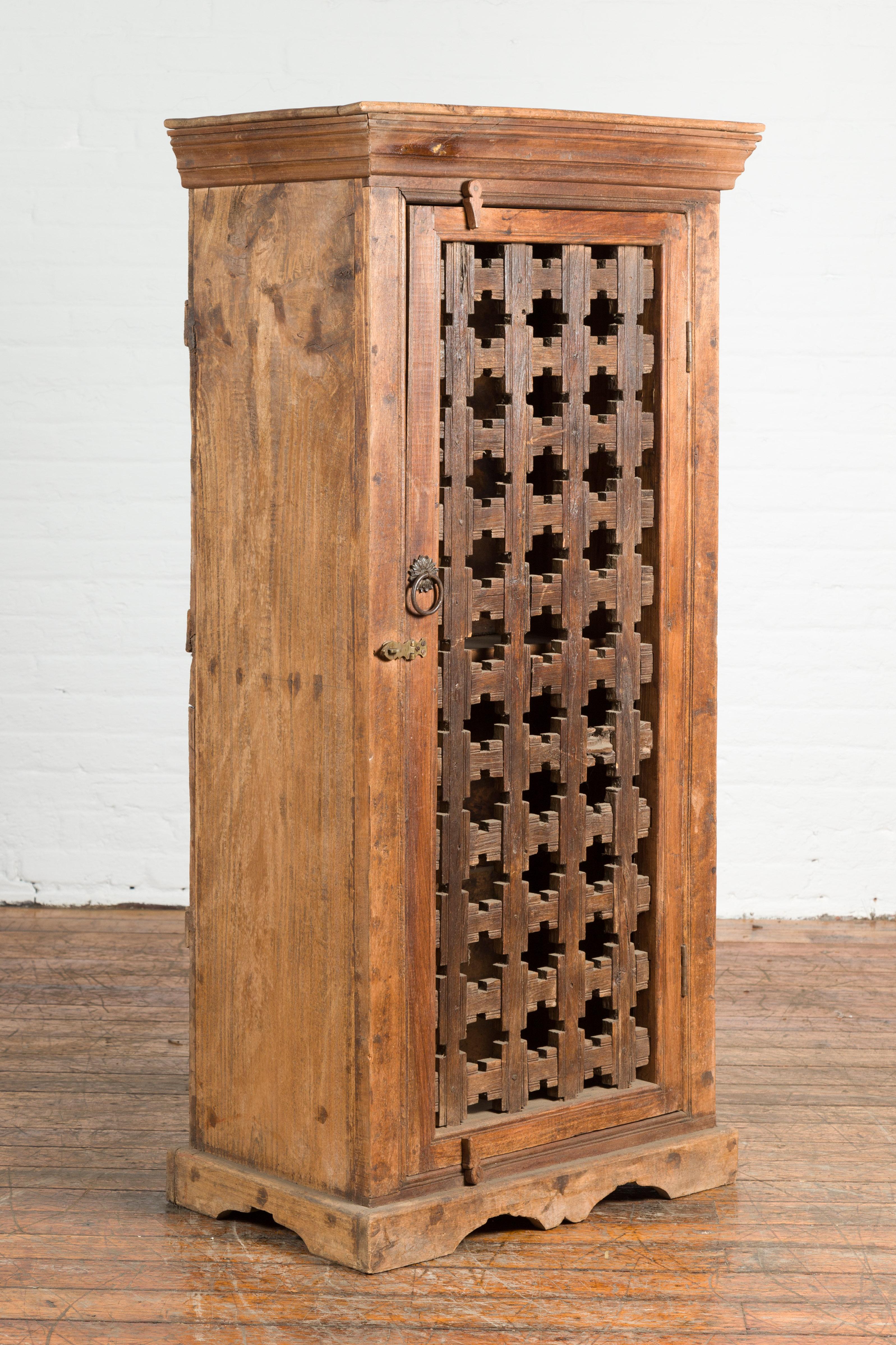 An Indian wooden cabinet from the 19th century, with single fretwork door and brass ring handle. Created in India during the 19th century, this wooden cabinet features a single door adorned with hand-carved geometric fretwork patterns. The piece is