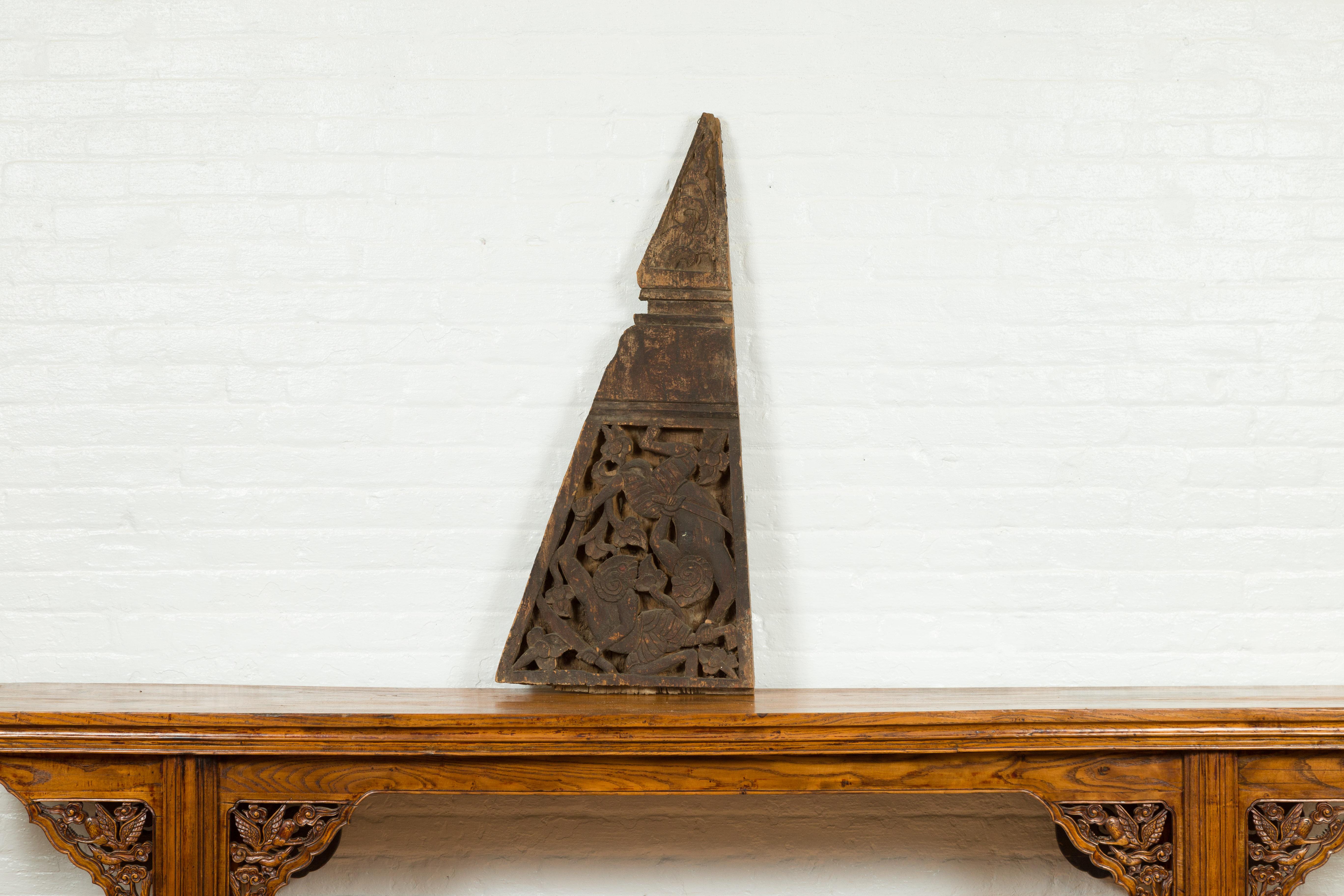 An antique Indonesian architectural hand carved wooden fragment from the 19th century, with mythical figures and triangular shape. Created in Indonesia during the 19th century, this architectural fragment features a triangular shape adorned on the