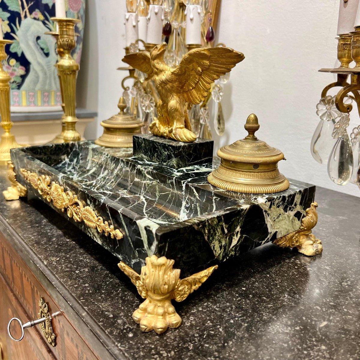 Nous vous présentons ce magnifique encrier de style Empire du XIXe siècle, d'époque Napoléon III, orné d'un motif d'aigle impérial en relief placé entre les deux encriers tenus par des supports en bronze doré. Le marbre de Portoro, l'un des plus