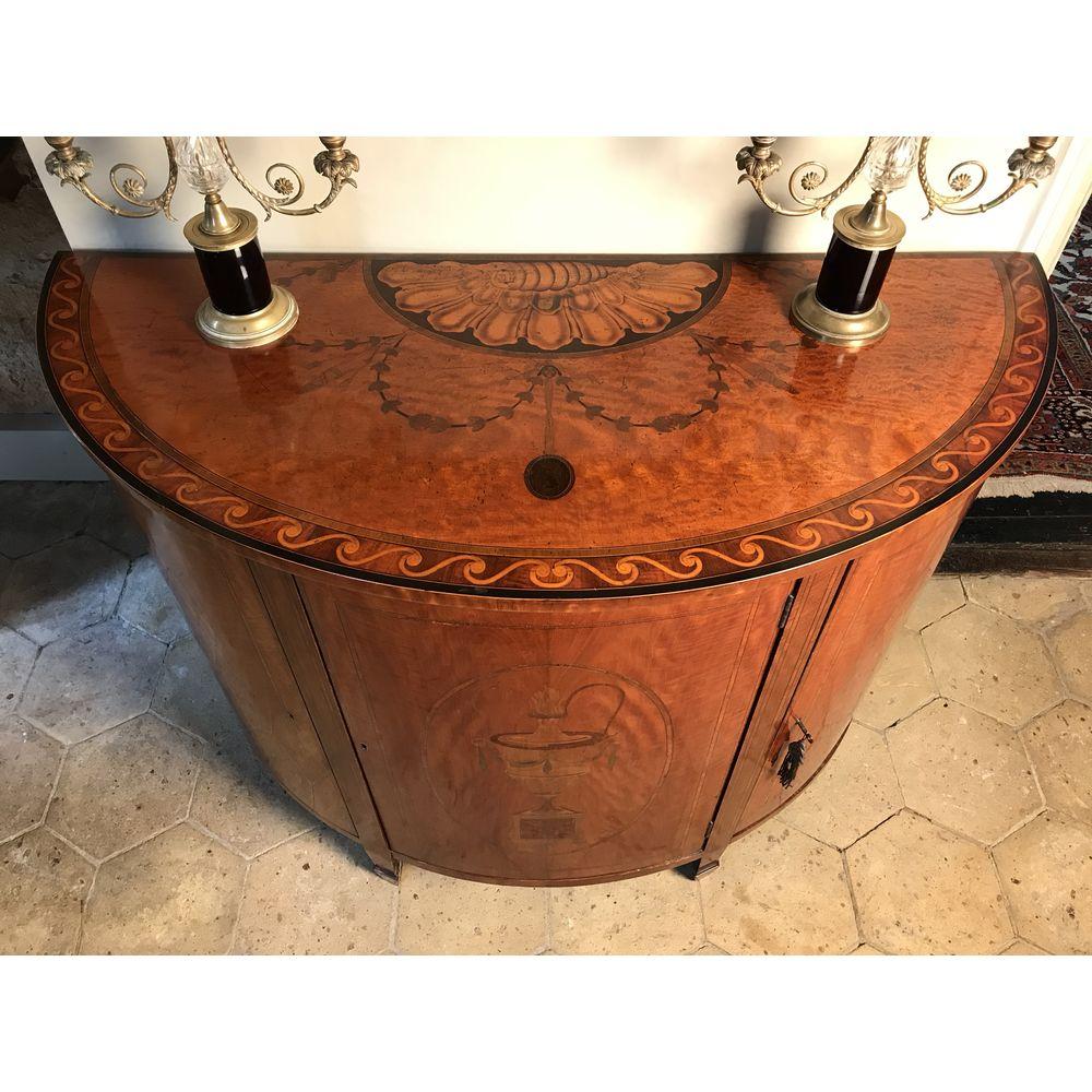 An English semi-elliptical, or demilune (half moon), inlaid satinwood commode of neoclassical form. 
Of very good rich color and patination.

The marquetry in kingwood, tulipwood, burr veneers and harewood. 
The fine quality top inlaid with a large