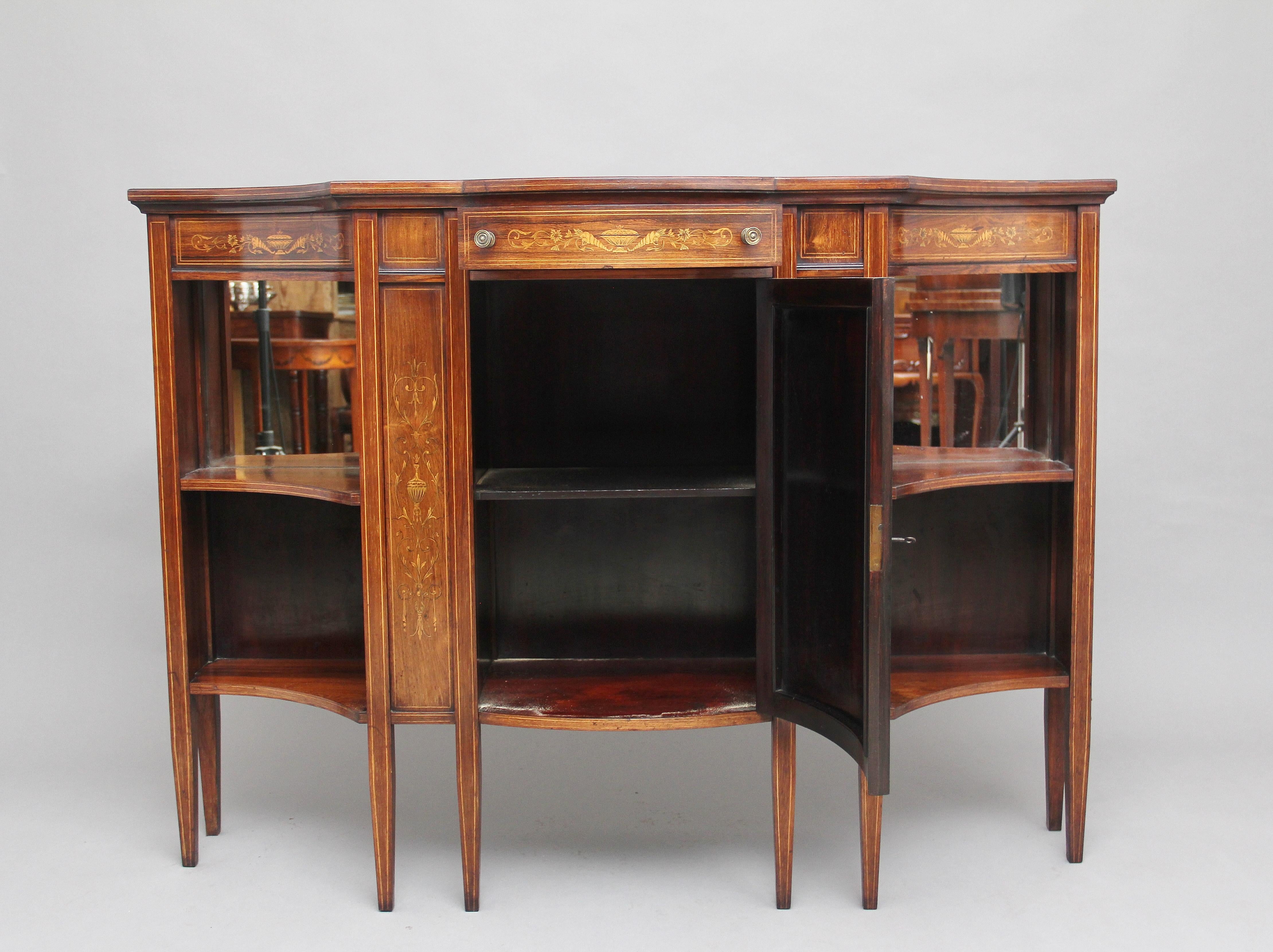 19th century inlaid rosewood cabinet of serpentine form, the shaped and wonderfully figured top above an inlaid frieze consisting of floral and urn decoration, a frieze drawer at the centre, mahogany lined with original brass turned knobs, below
