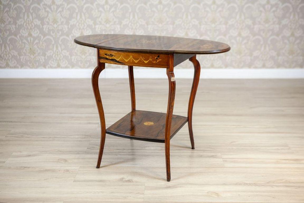 19th-Century Inlaid Rosewood Tea Table

We present you an inlaid Pembroke tea table with foldable leafs.
The extendable oval top is placed on bent legs. In the bottom section, there is a delicate ornate shelf.
This rosewood piece of furniture is