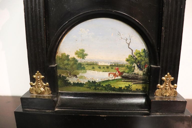 Rare and fine quality table clock pendule. The clock is made of painted wood. On the front above a precious inlay with pearl. In the lower part a hand painted miniature landscape with knights. Some finely chiseled gilded bronze decorations