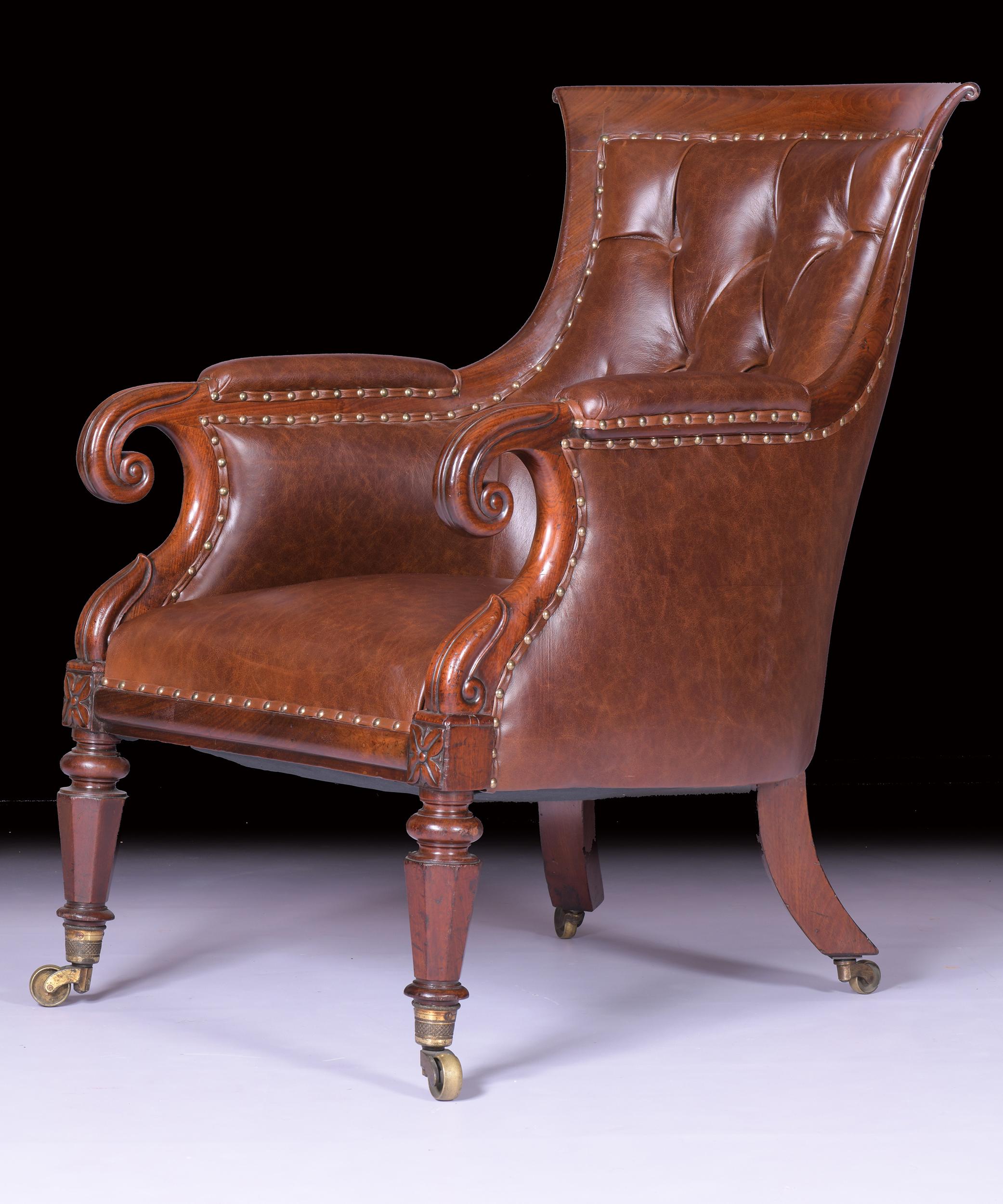 A very fine early 19th century mahogany framed library armchair, the curved top-rail above button back upholstered in leather, with raised padded arm rests and down scrolled arms which sit above the front turned legs and brass wheel casters, the