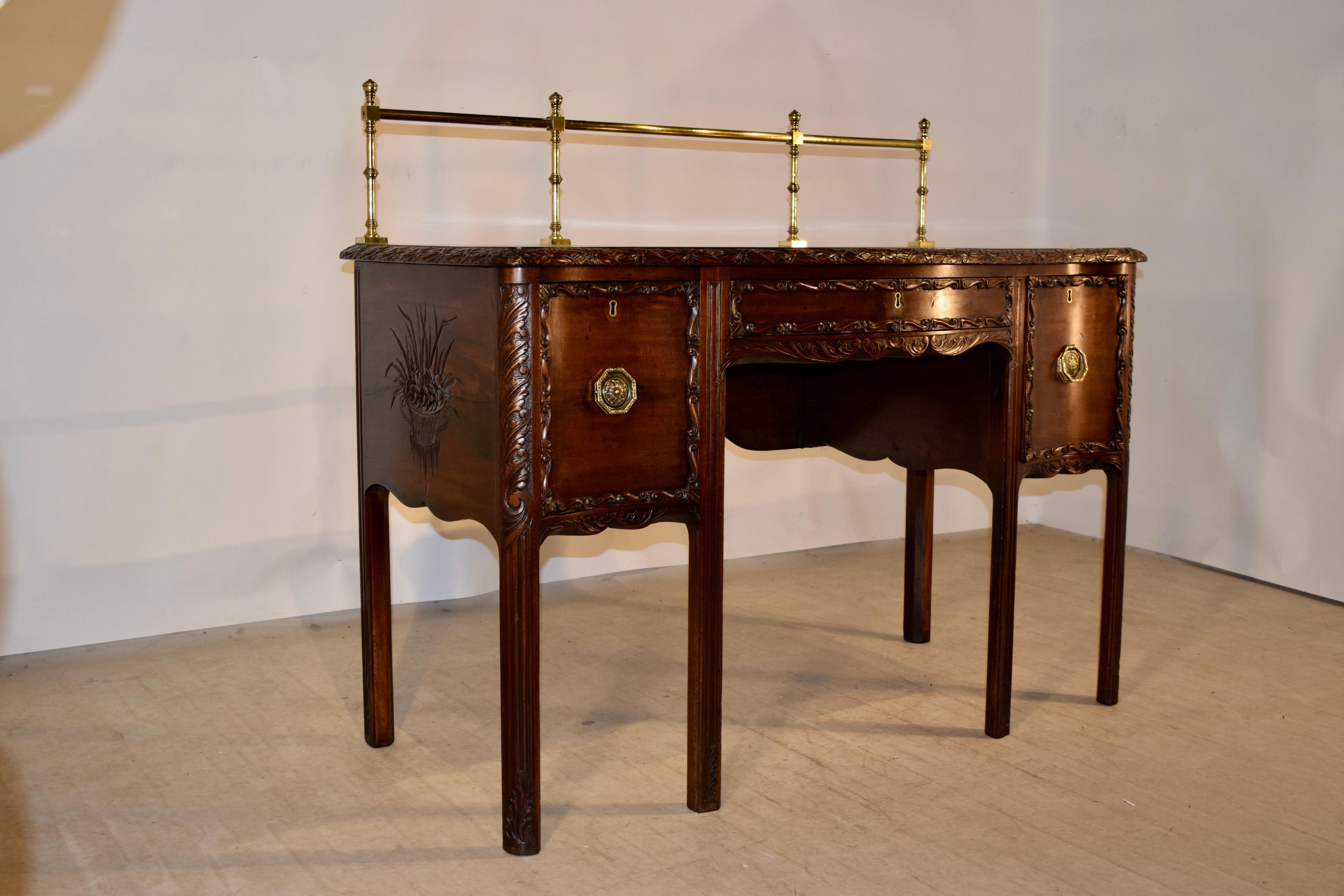 19th century Irish sideboard made from mahogany with a lovely hand cast brass decorative railing on the top, following down to a richly grained top with a beveled and hand carved edge depicting ribbons and floral. There is a single drawer flanked by
