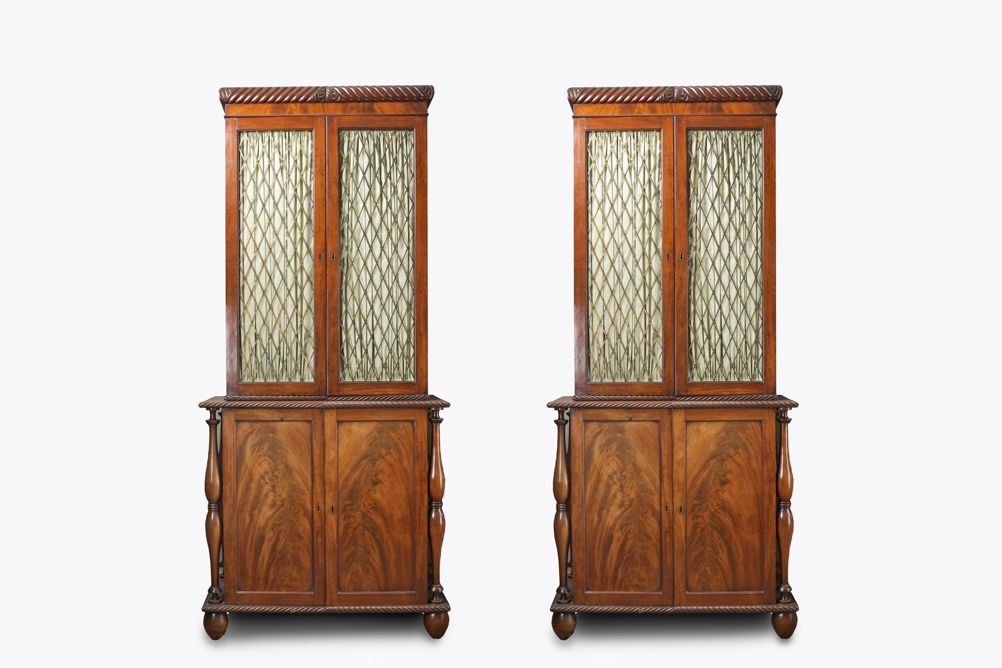 19th century Irish pair of cork flame mahogany bookcases, the upper section with stepped cornice with carved rope twist and acanthus flower motif raised above two brass grille lined doors with rope twist detail opening to reveal shelved interior.