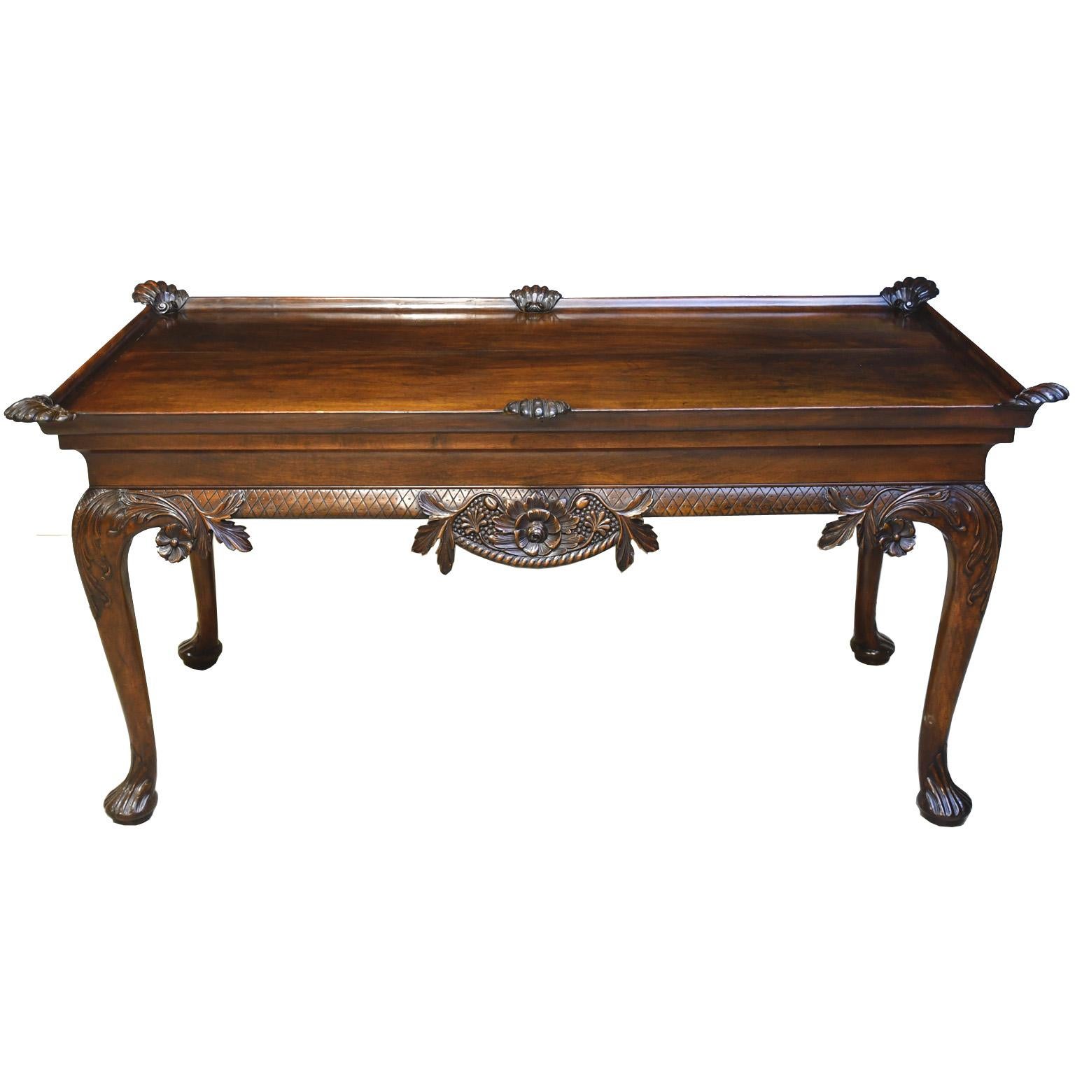 An exquisite Irish library table in fine mahogany dating from the first half of the 1800s in the Queen Anne revival style with exceptional carvings of rococo motifs. A long rectangular tray-board top embellished with coquillage or carved scallop