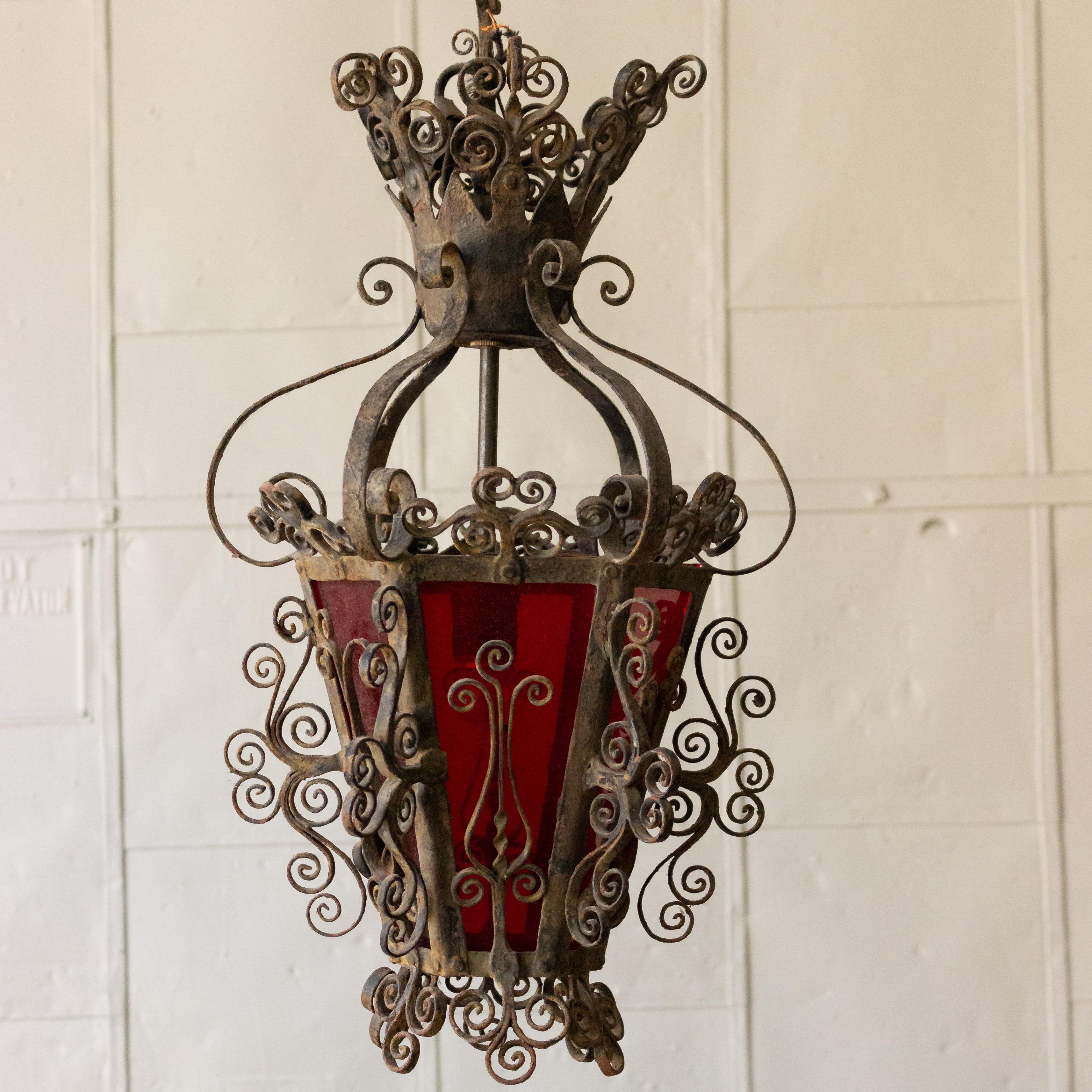 Highly decorated and scrolled iron lantern with red glass panes. The original black paint finish is distressed but still very much visible.
