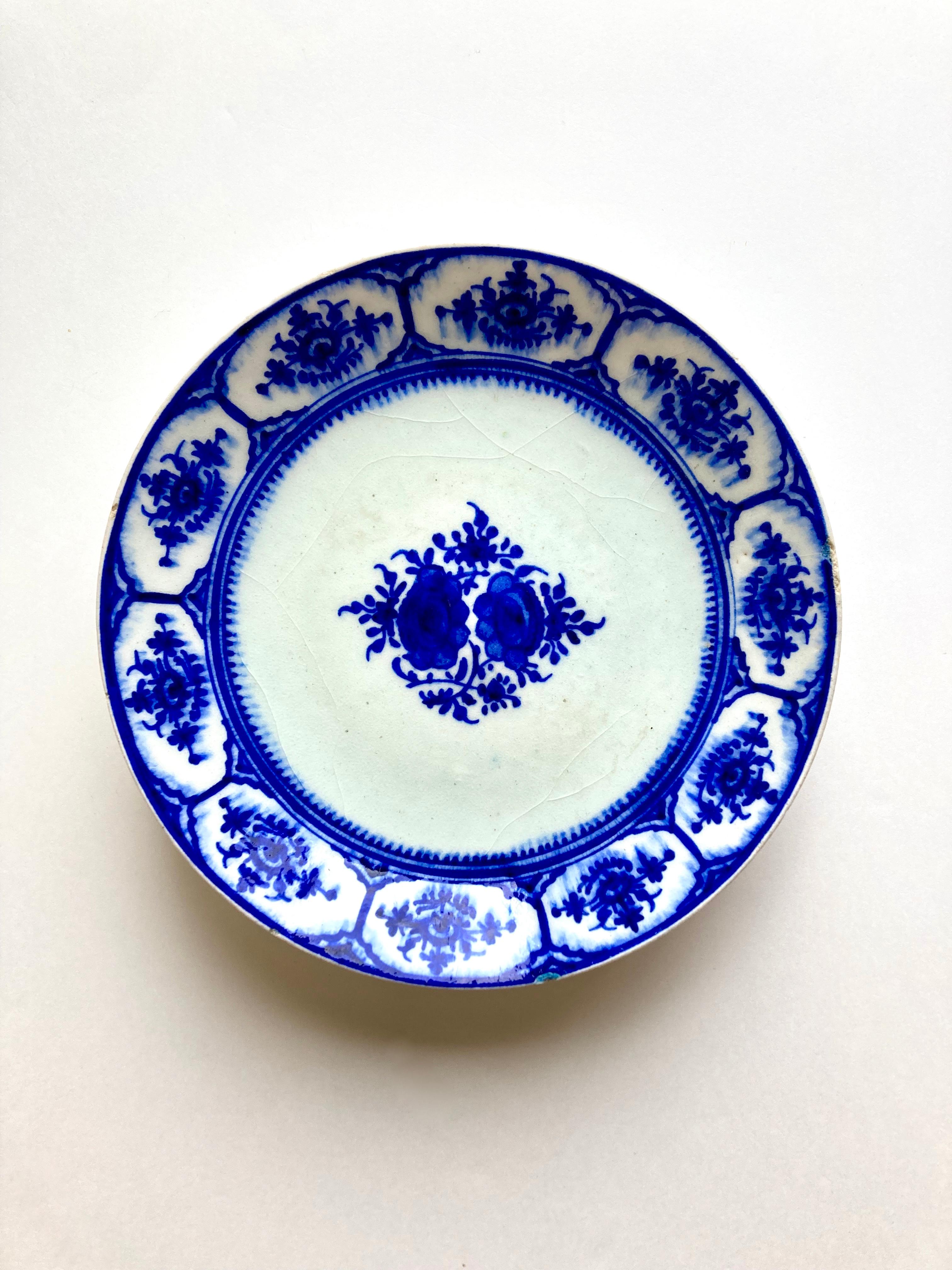 Une mystérieuse assiette ancienne en poterie bleue et blanche. Il s'agit d'une assiette en faïence, peinte à la main d'un motif floral en bleu de cobalt sous glaçure, peut-être une imitation d'une composition chinoise ou même européenne/de Delft.