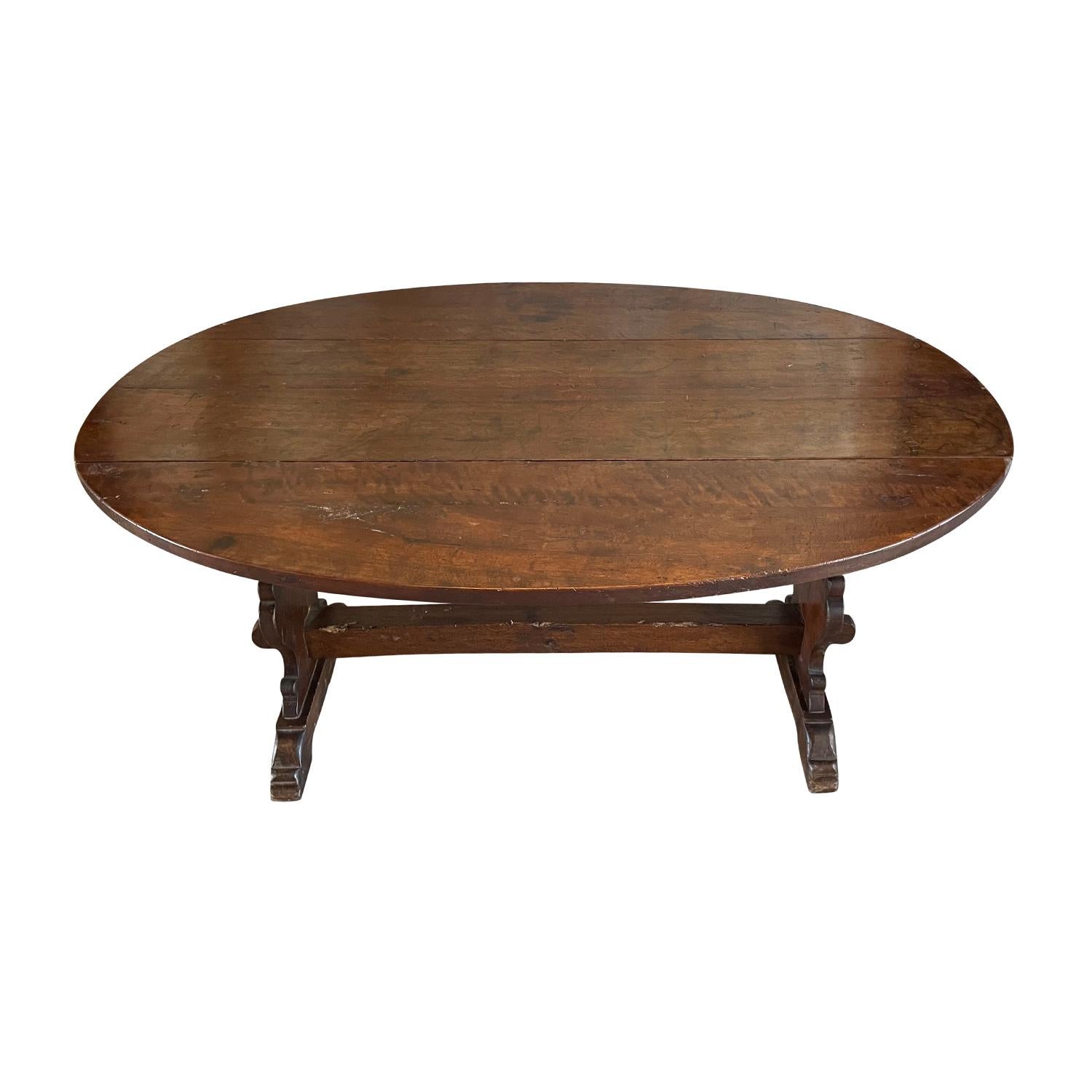 An antique Italian small oval dining table with hand waxed finish. This Tuscan table is made of hand crafted Walnut and supported by a substantial trestle design base, in good condition. The two sides of the dining room table are foldable. There is