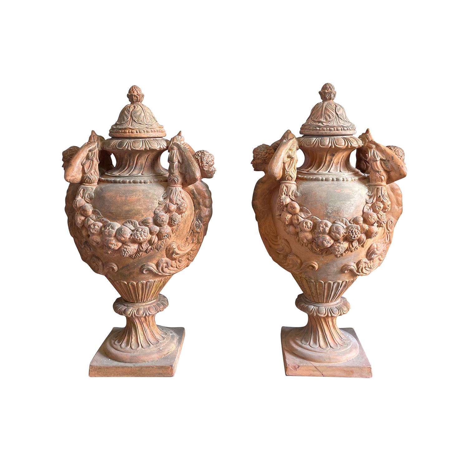 A pair of Renaissance style very ornate antique Italian terra cotta vases decorated with Caryatides and garlands, in good condition. The bodice of the urns is set on a square base. The finials are topped with a lid and with a pomme de pin finials.