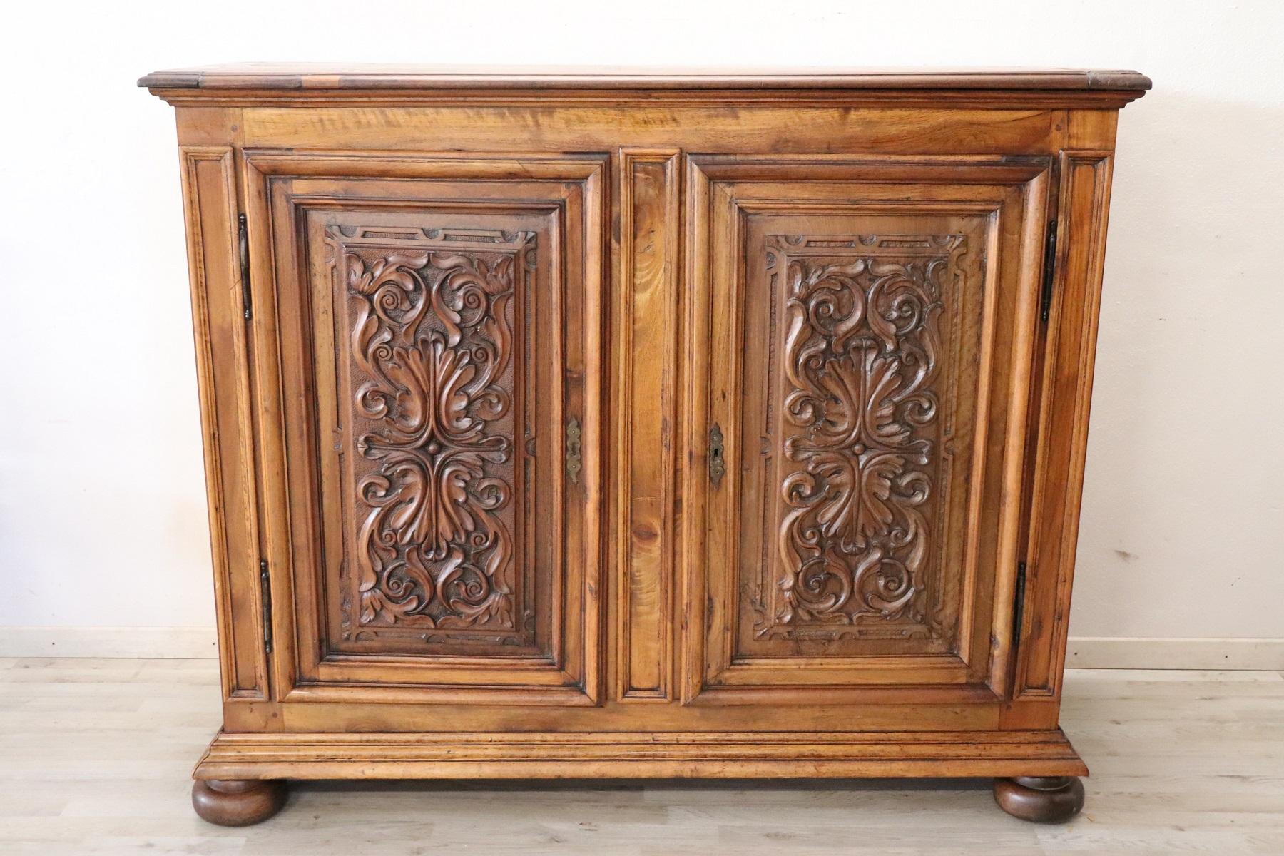 Important and rare antique solid walnut sideboard, 19th century. Characterized by a refined hand carving of the wood on the front doors. The fine walnut wood has acquired a beautiful old patina. Internally equipped with two shelves. Majestic and