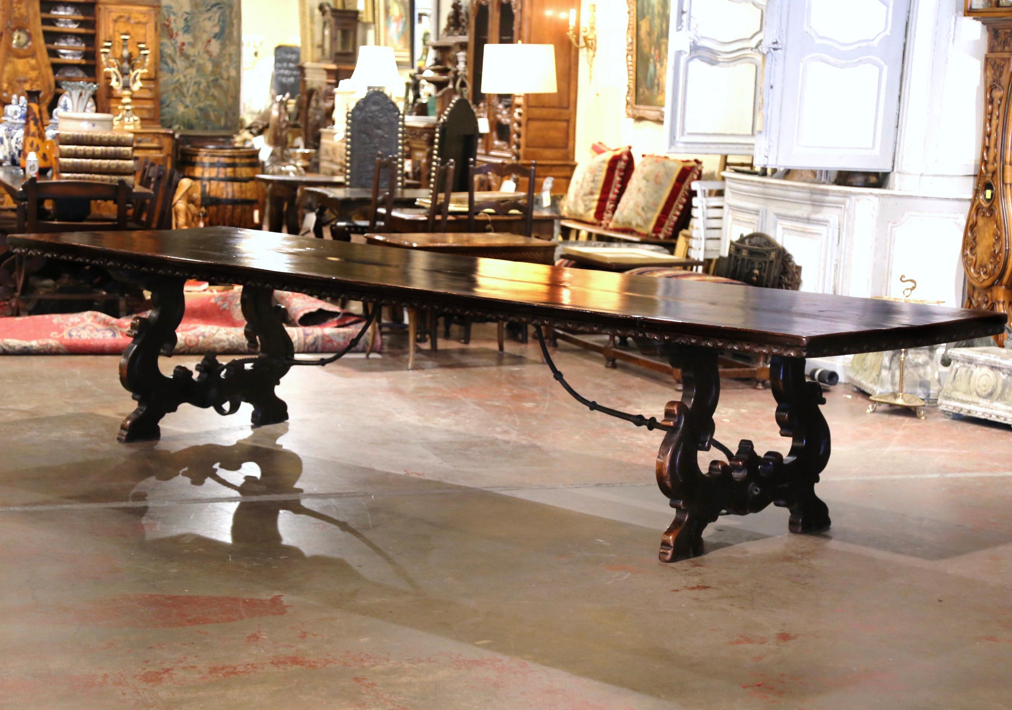 Entertain in style with this monumental 13 feet antique dining room table! Crafted in southwest Italy, circa 1860, and built in walnut, the large trestle table stands on hand carved scroll supports ending with paw feet, and joined at the legs with a