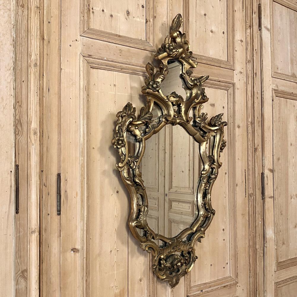 19th century Italian Baroque giltwood mirror is a splendid example of the genre, with sculpted wood frame and a finish glowing with the warmth of patinaed gold. Floral and foliate adornments permeate the design, with an intricately contoured frame