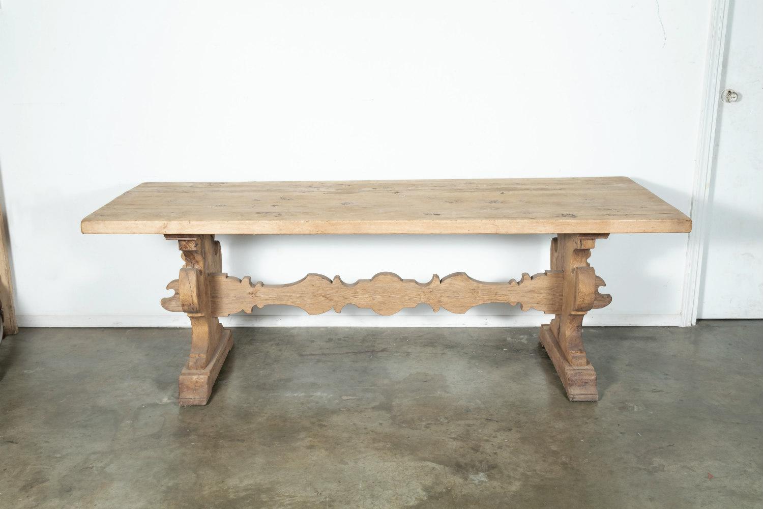 A handsome 19th century solid chestnut Baroque style bleached trestle farm house table handcrafted in the Tuscany region having a rectangular plank top raised by two thick carved urn shaped supports resting on plinth bases joined by an impressive