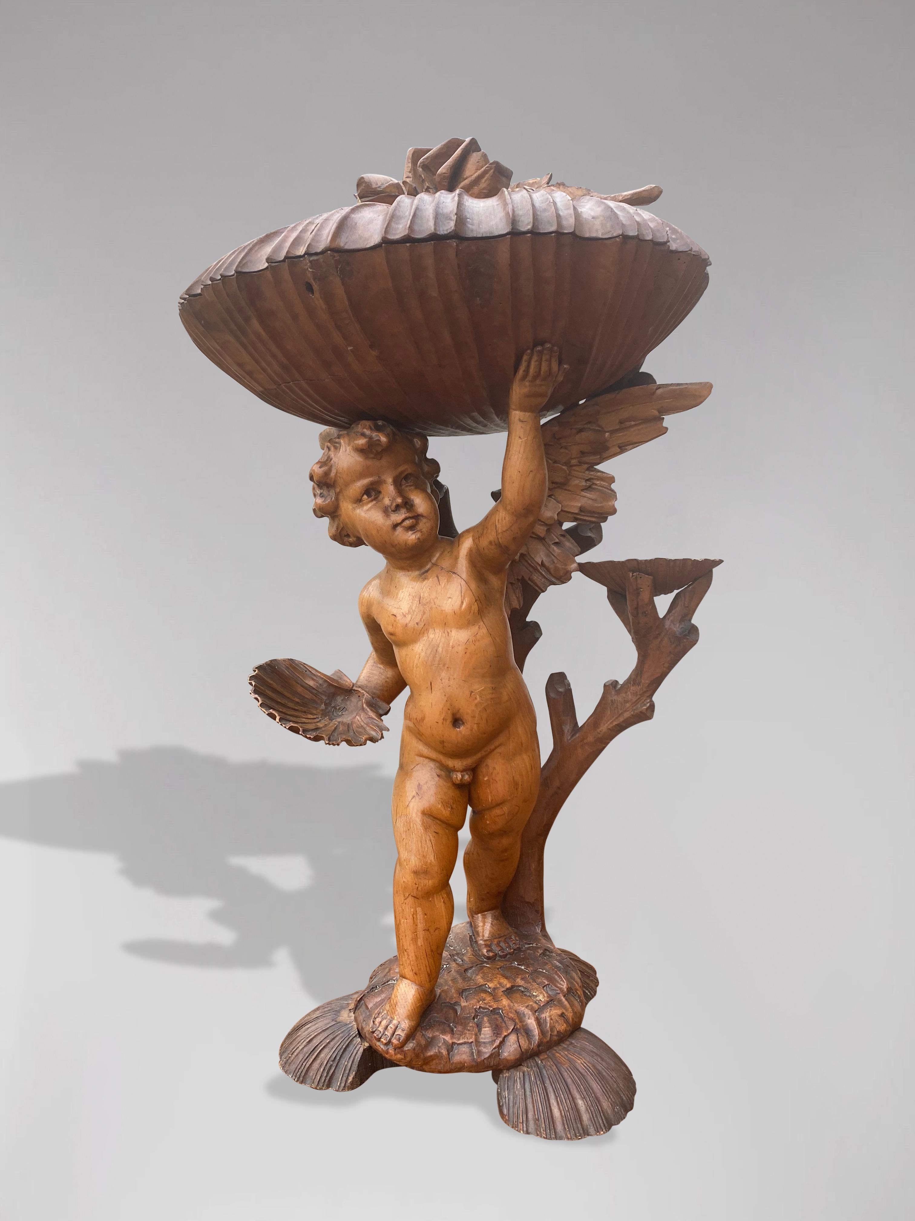 A 19th century impressive large scale Italian Baroque style putti statue, depicts a winged cherub, with branch, different smaller scallop shells and holding one large carved scallop shell in exceptional detail, lovely patina and hand carved into