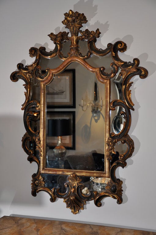 Miroir de style baroque italien, doré à la feuille et ébonisé. Les plats marginaux sont entourés d'une bordure principale en cartouche décorée de têtes de fleurs et de C-scrolls surmontés d'une urne de fleurs.