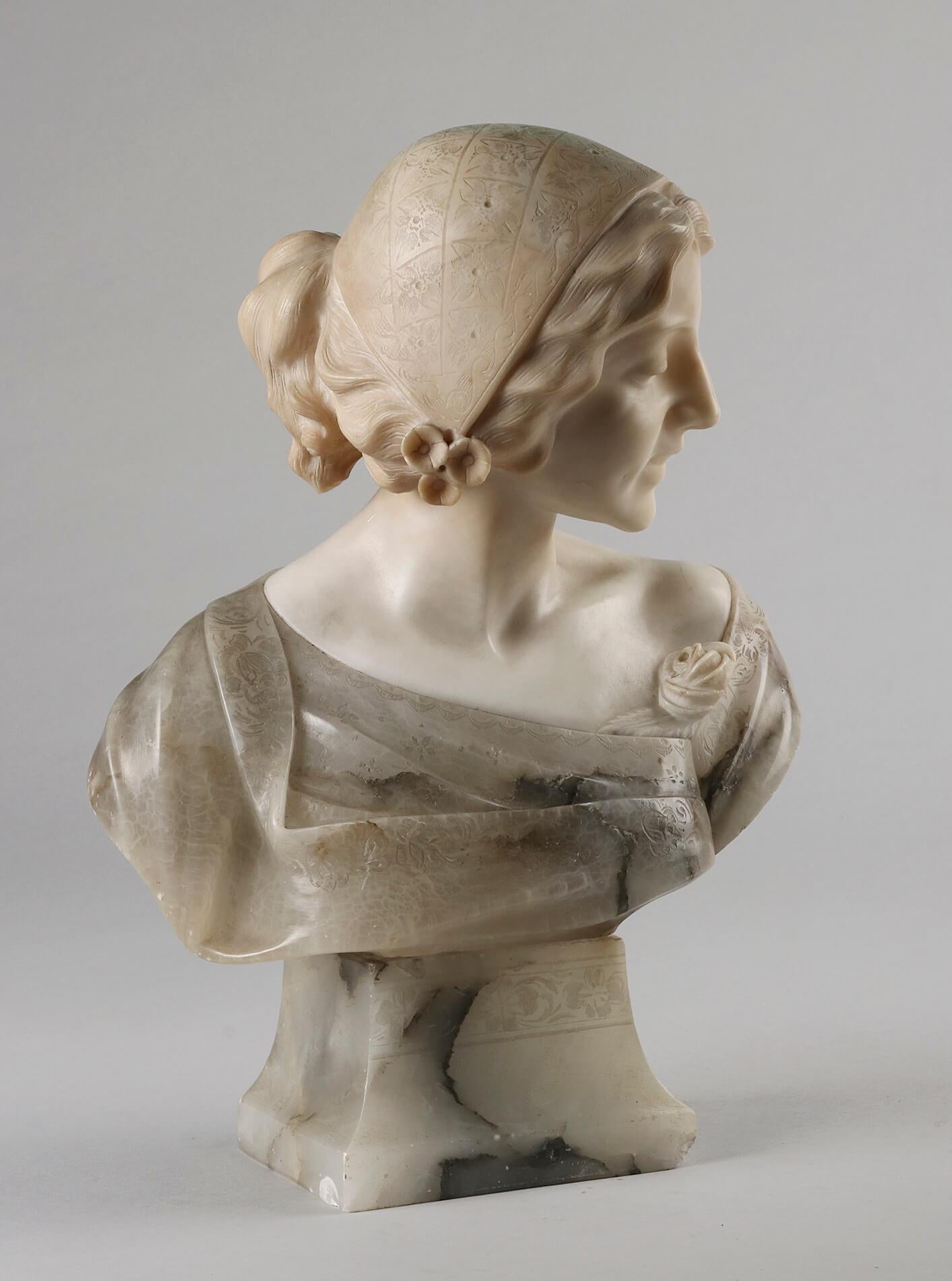 Beautiful antique bust of a girl. The statue is made of different types of alabaster. The girl has a serene, subdued smile. She wears a rose on her dress. The statue has a special appearance. There is a small damage on the corner of the foot. This