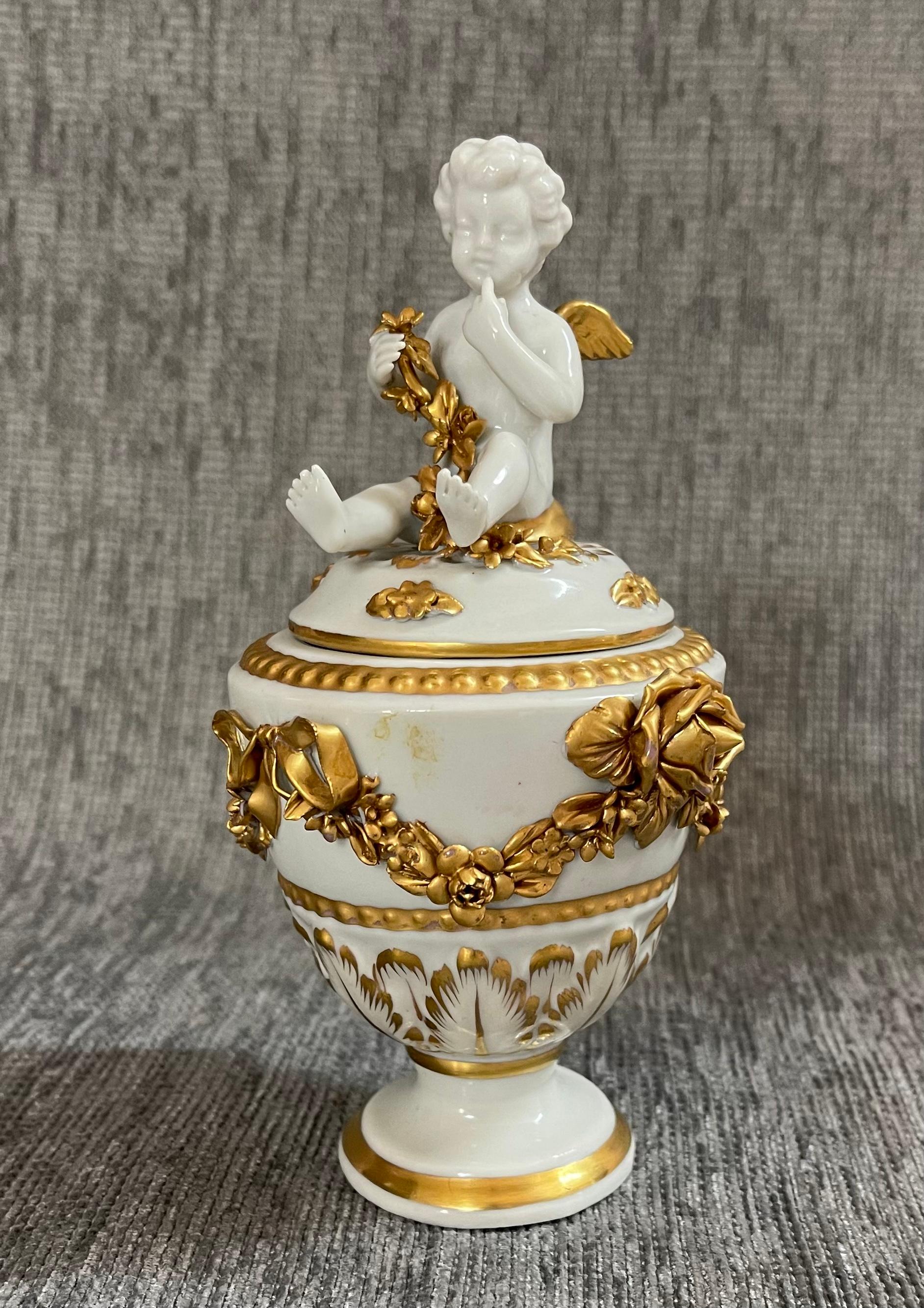 Capodimonte White and Gold Porcelain Vase 
A beautiful, important white porcelain vase from the prestigious Capodimonte porcelain manufactory. 
It features at the top a delightful cherub in the act of bringing a finger to his mouth.
What makes this