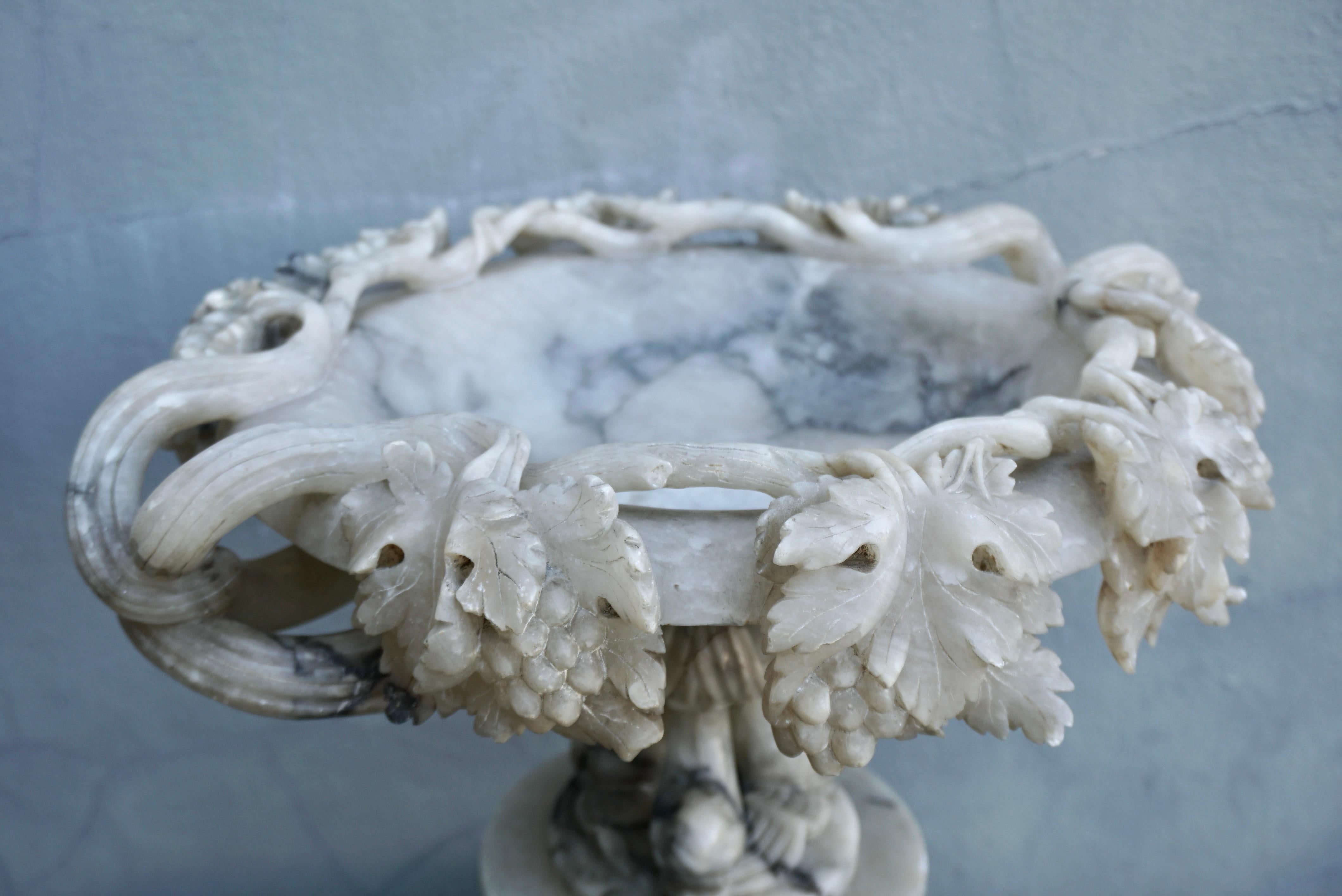 Beautiful and rare antique Italian alabaster tazza compote. Features carved grape leaves around the bowl and dolphin pedestal.

Decorate a dining table or a console with this elegant antique centrepiece. Created in Italy circa 1900 and made of