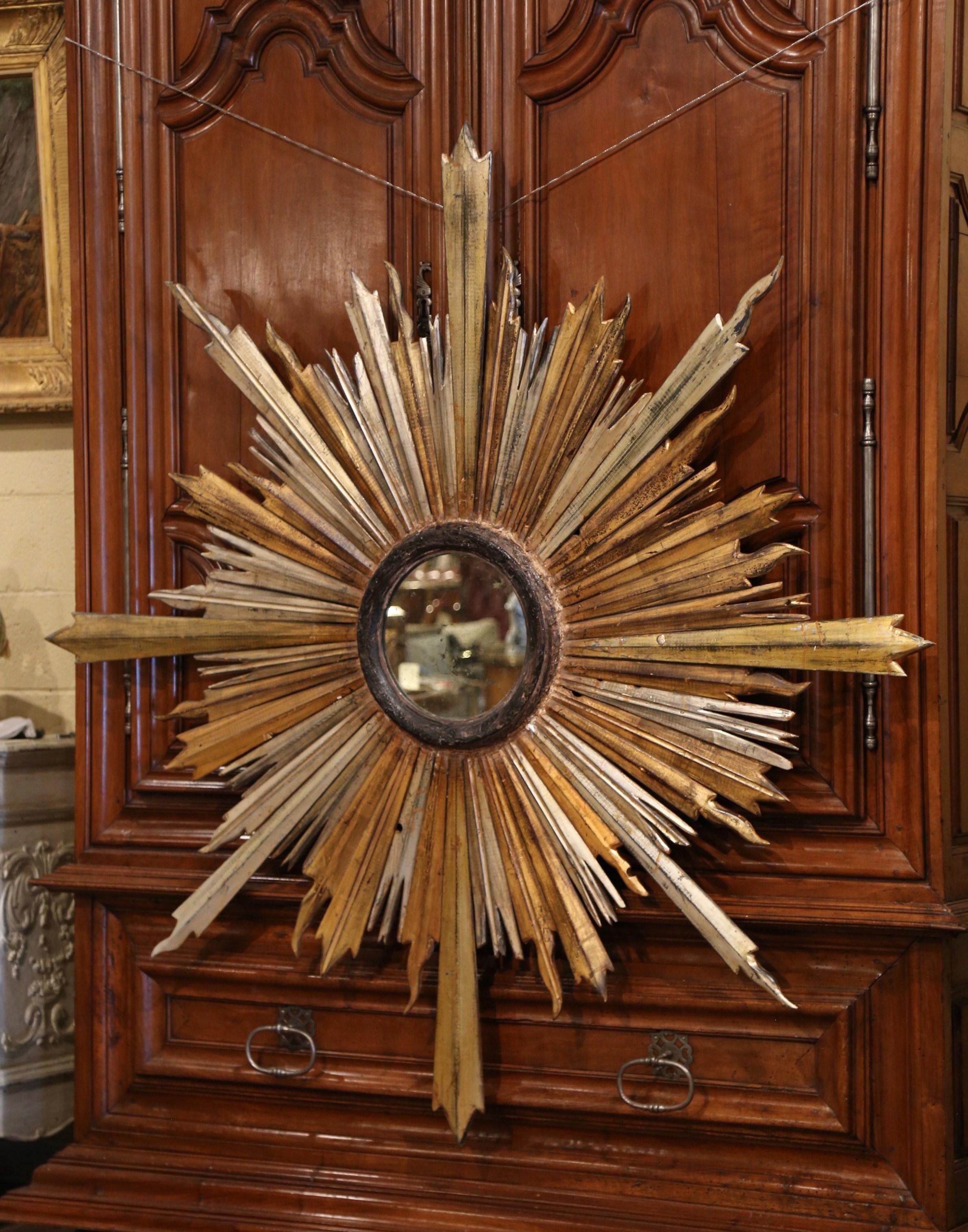 This important antique sunburst mirror was crafted in Italy, circa 1890. Over five and a half feet wide, the monumental, stand-out piece features high relief carved decorative gilt and silvered sun beams around a circular center mirror with its