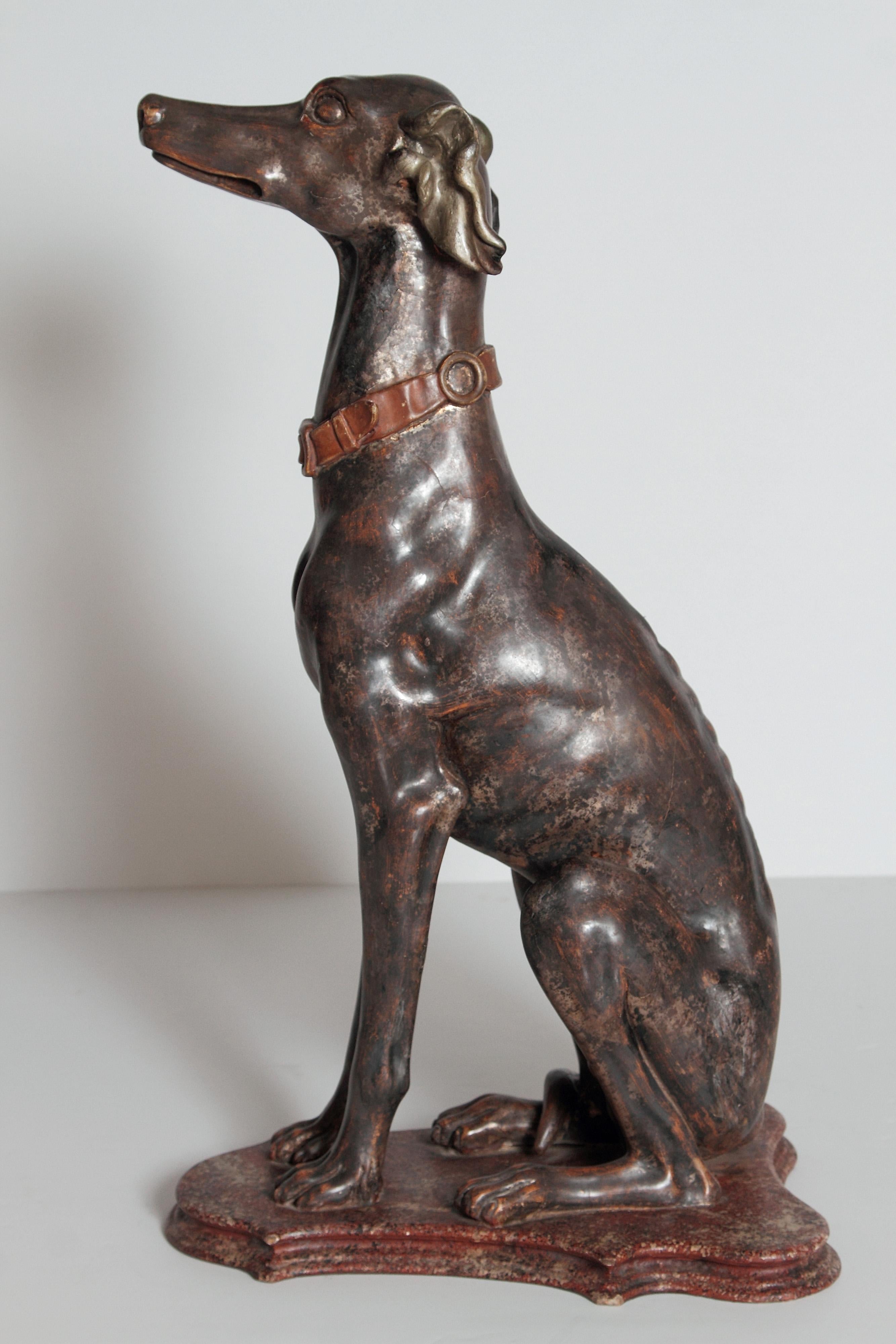 A fine example of a tall Italian greyhound sculpture from the 19th century. The greyhound is sitting attentively on a painted faux marble base. Painted in brown with skillful attention the head, ears, body and paws around which the tall is wrapped.