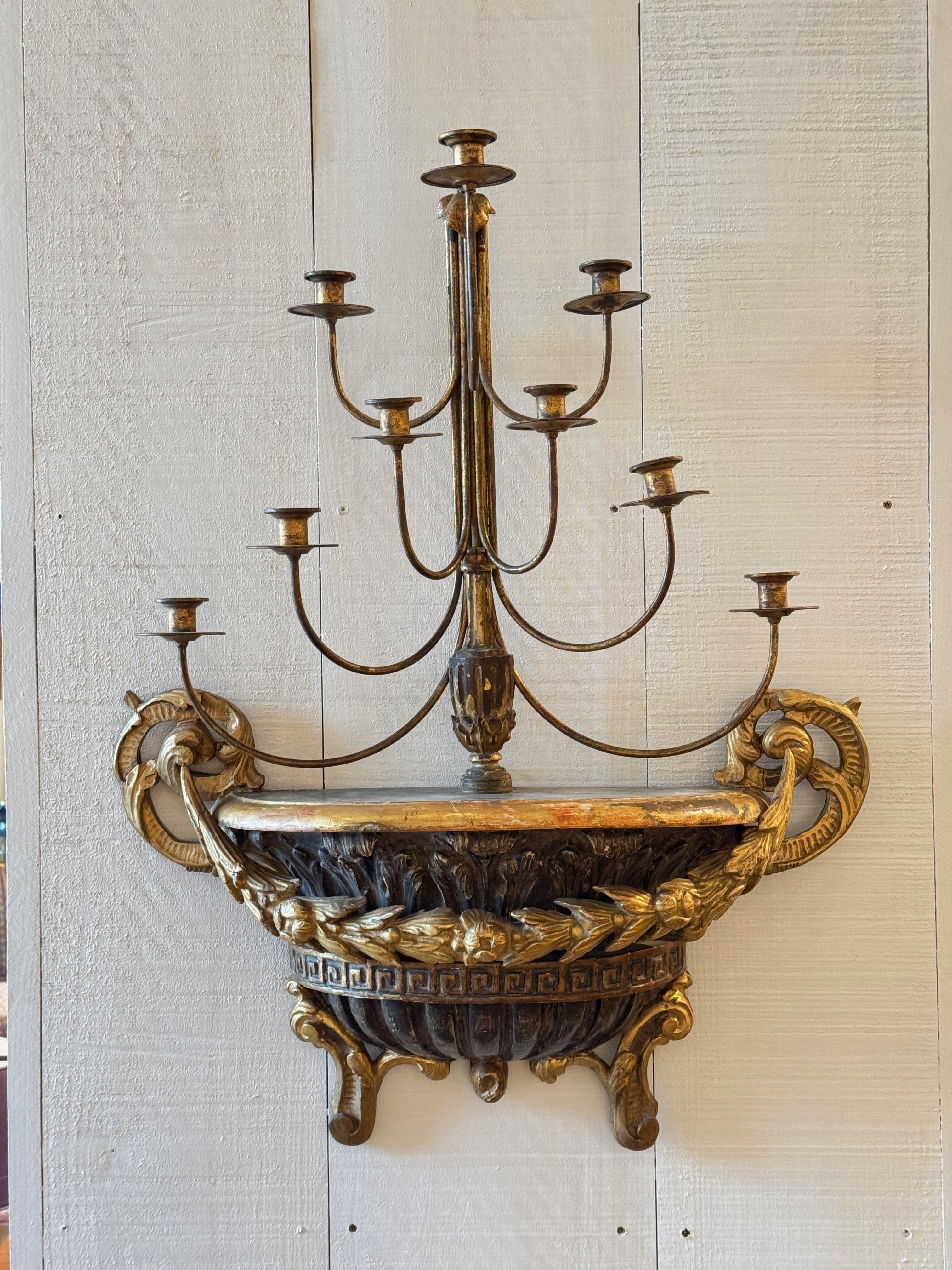 Dramatic and sculptural Italian wall sconce, , featuring a carved urn base with classical motifs and a multi-arm candelabra form. The sconce is richly detailed with acanthus leaves, scrollwork, and a Greek key band, all finished in a weathered black