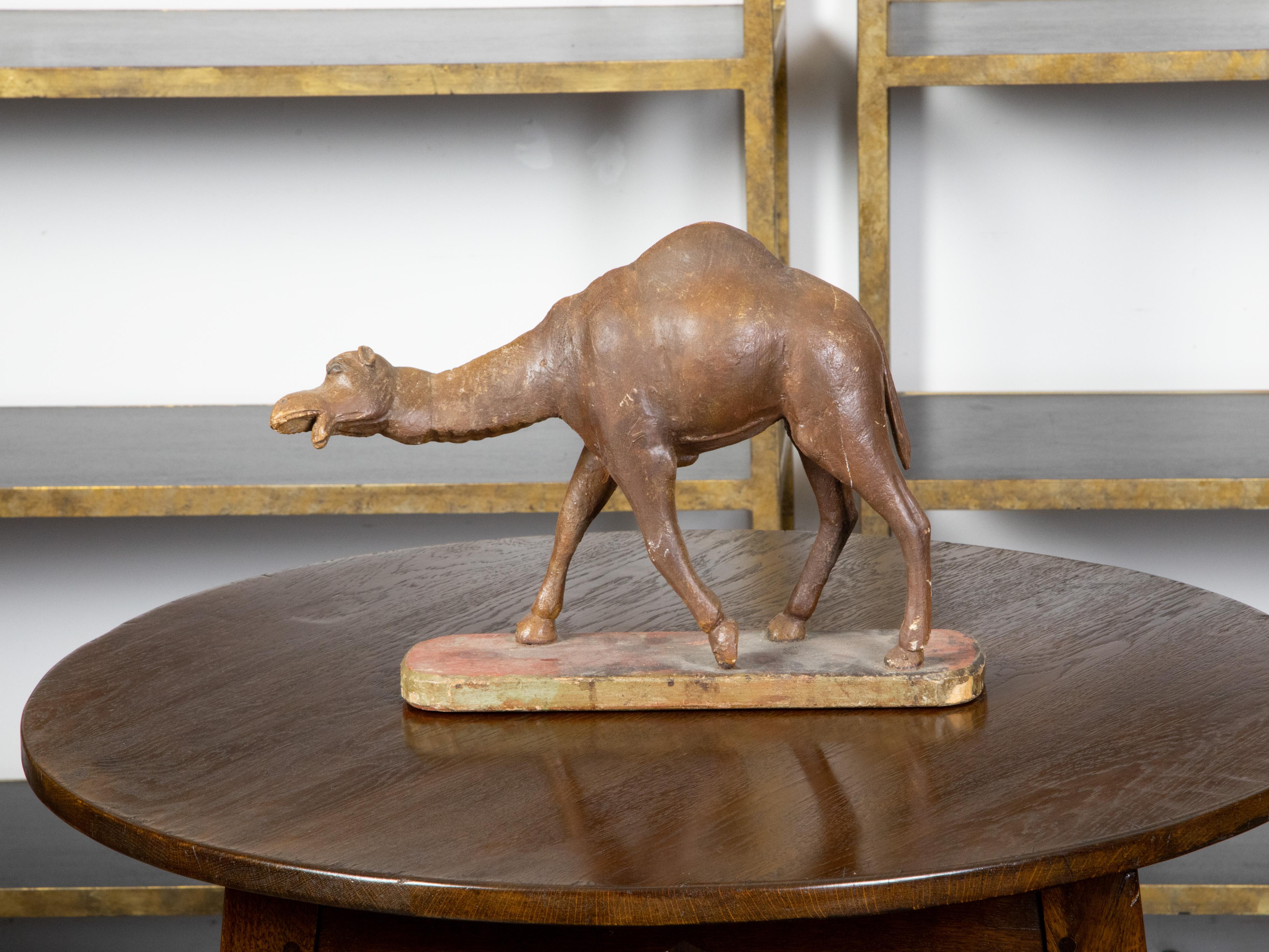 An Italian carved wooden camel from the 19th century, with oval painted base. Created in Italy during the 19th century, this carved wooden sculpture depicts a dromedary camel with single hump, standing on an oval painted base with red accents.