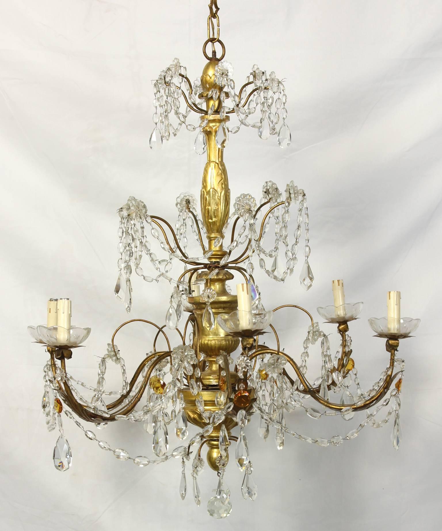 An Italian giltwood and crystal six-light chandelier dating from the early 19th century. The chandelier features a central giltwood staff adorned with gilt iron arms draped with swags of clear and amber crystals.