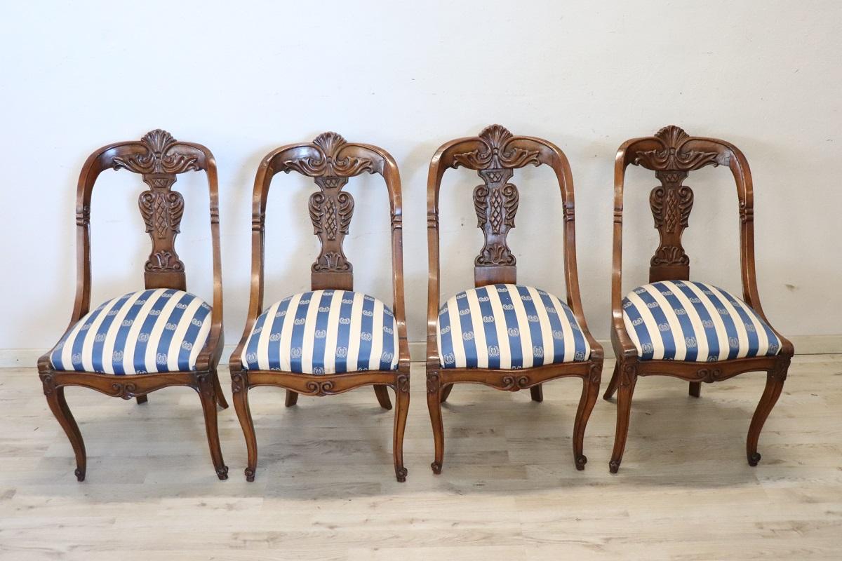 Precioso conjunto de cuatro sillas antiguas de madera maciza de nogal del siglo XIX de la época Carlos X italiano. Se caracteriza por un respaldo envolvente y refinado, embellecido con una elaborada decoración tallada a mano en madera de nogal. El