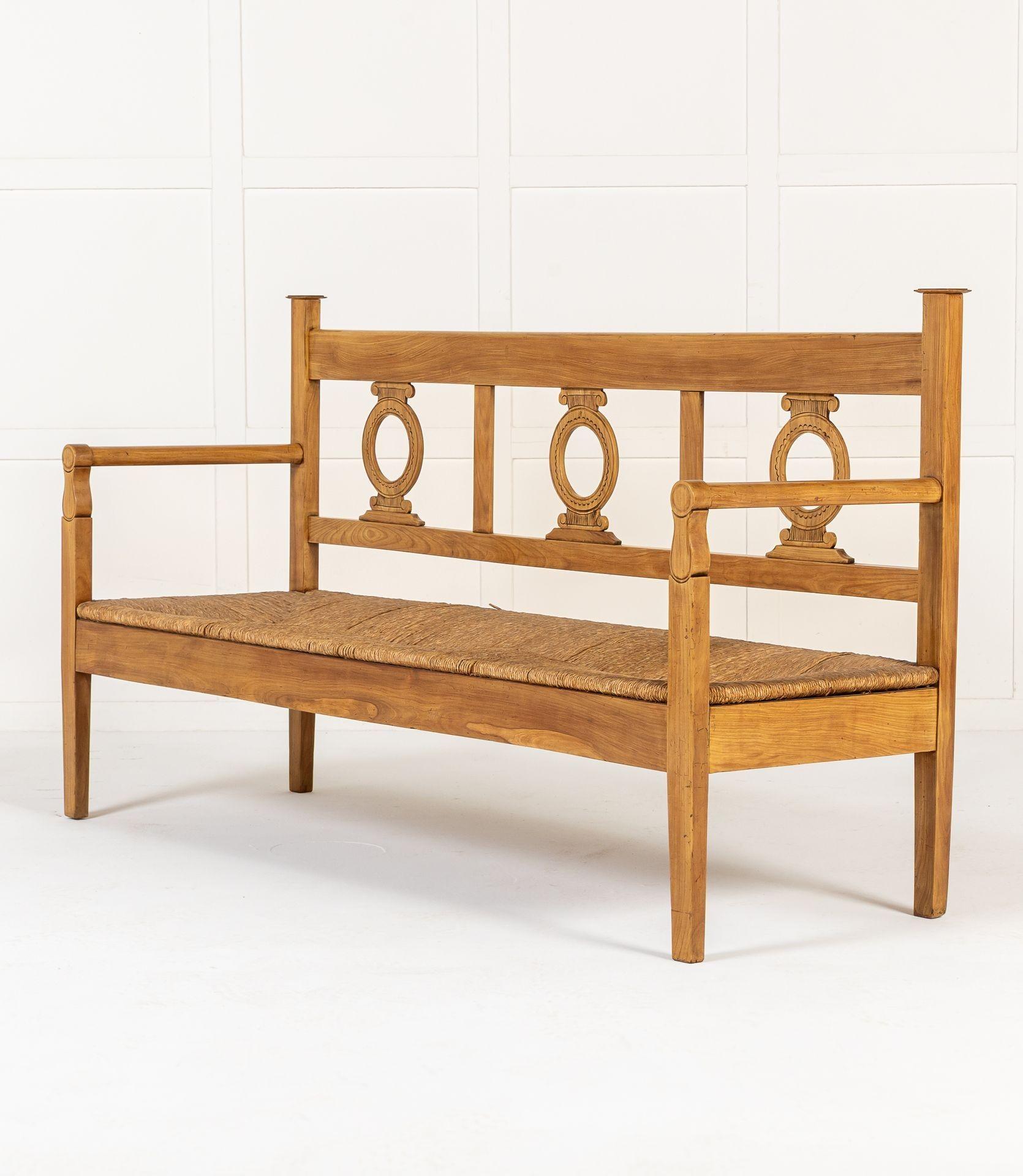 19th Century Italian cherrywood three-seater bench with rush seat. Each of the three chair backs have classical capitals framing central fretted circles, all with penwork detailing. The back rails are flat adjoining turned arm supports. The bench