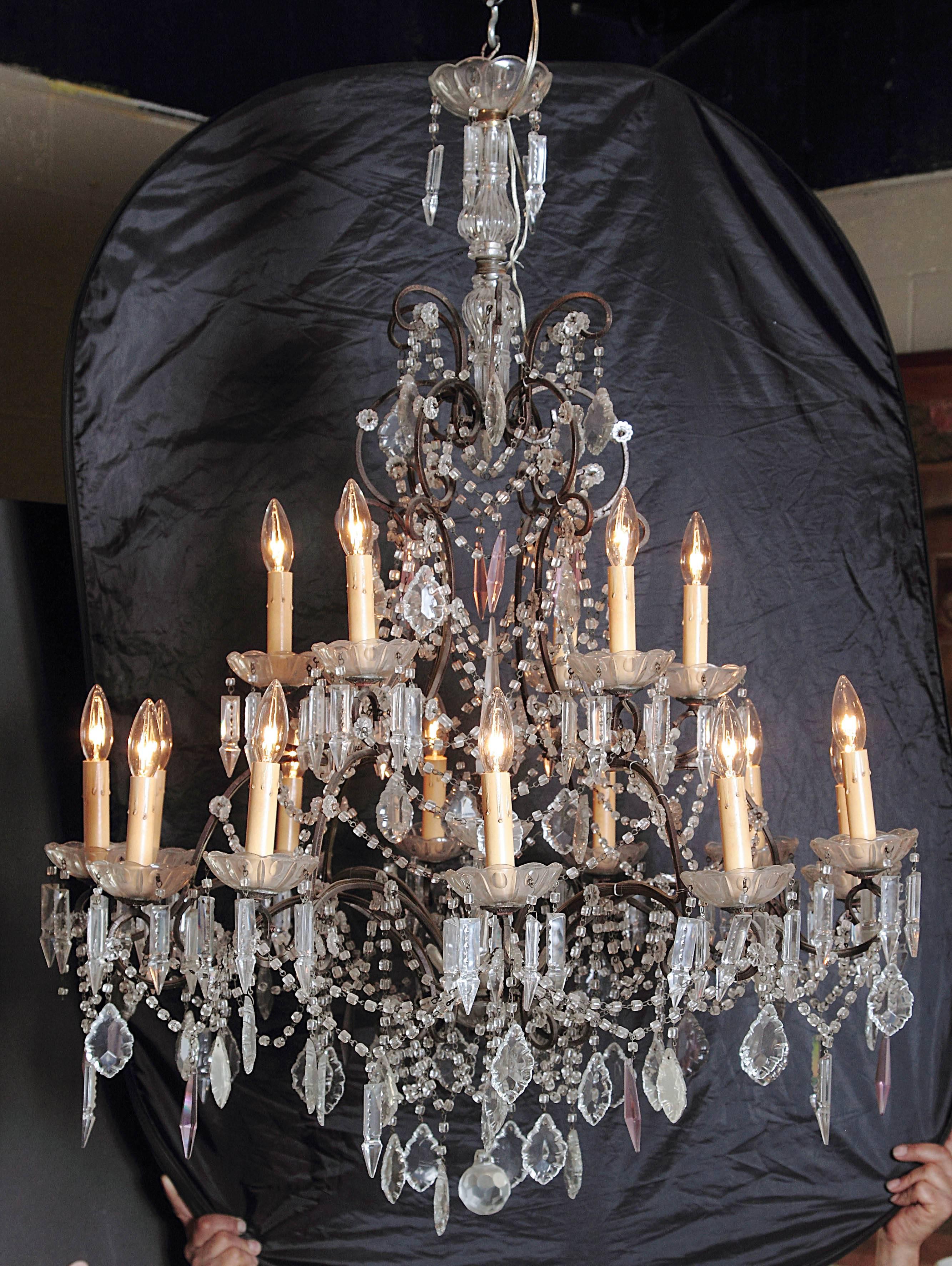 This elegant crystal and iron light fixture was created in Italy, circa 1890. The intricate chandelier has eighteen candlestick lights on two graduated tiers with luxurious swags of crystal and glass pendants hanging throughout. The beautiful,
