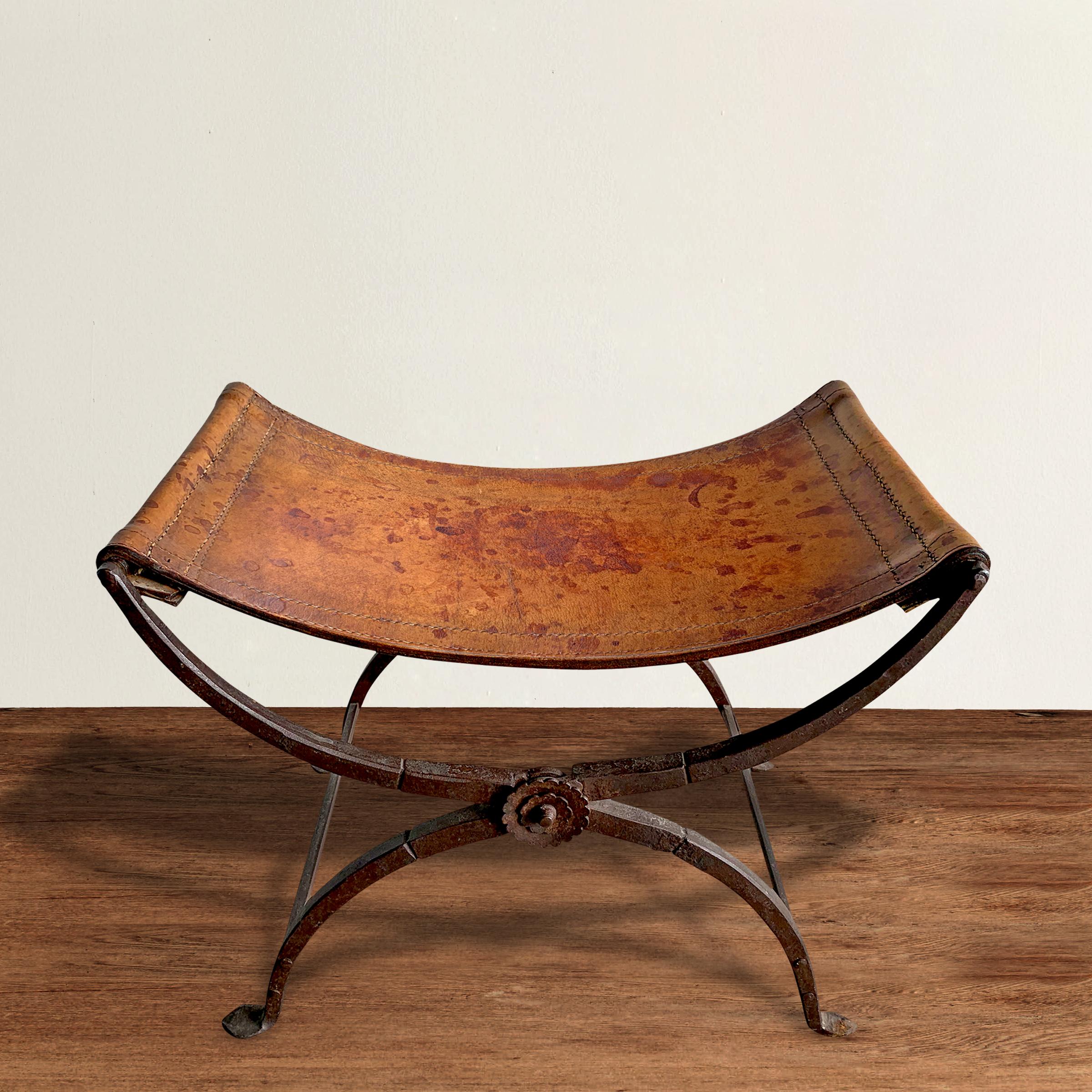 A striking 19th century Italian wrought iron folding Curule stool with a handstitched saddle leather seat and decorative floral rosettes on both sides where the legs cross. Curule seats were designed by early Romans and were seen as a symbol of