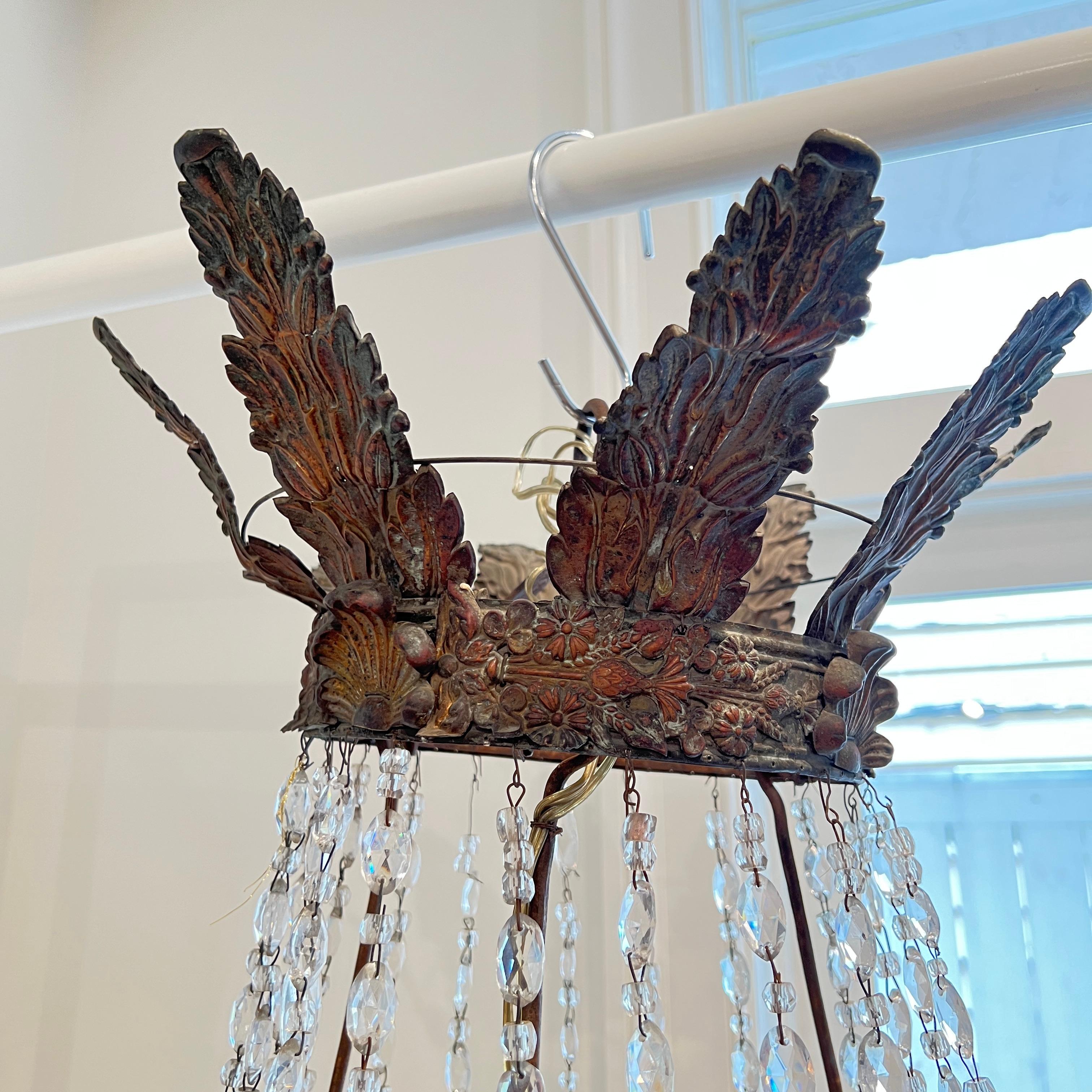 This exquisite 19th century Italian Empire chandelier from Bologna features a finely gilt iron frame adorned with cascading hand-cut crystal drops and swags. The metal accents are richly detailed using the repousse technique, adding depth and