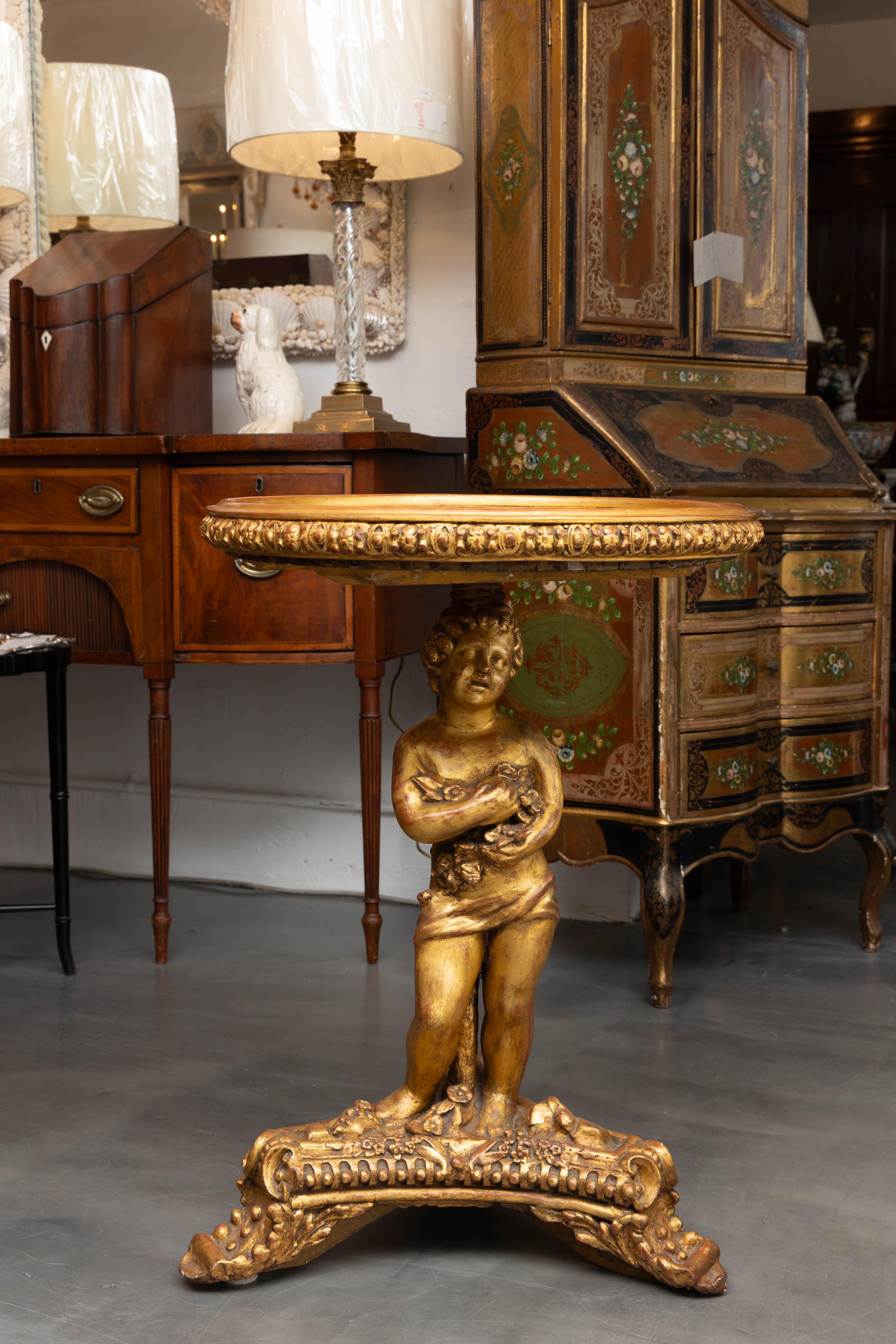Il s'agit d'un putto italien du XIXe siècle en bois doré, sculpté à la main, qui sert de piédestal à un plateau de table incrusté de divers carrés de marbre dans le style d'un échiquier.  Le sommet est encadré par un cadre circulaire sculpté et le