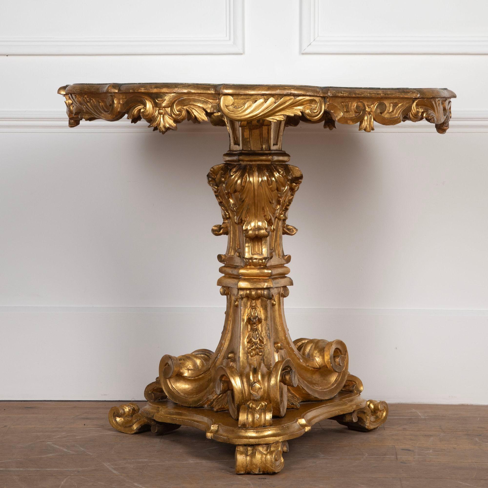 Élégante table centrale du début du 19e siècle. Le plateau en marbre simulé avec bord moulé et frise sculptée d'acanthes, repose sur une élégante base triforme en bois doré avec des volutes exagérées, une sculpture de feuillage, et se termine par
