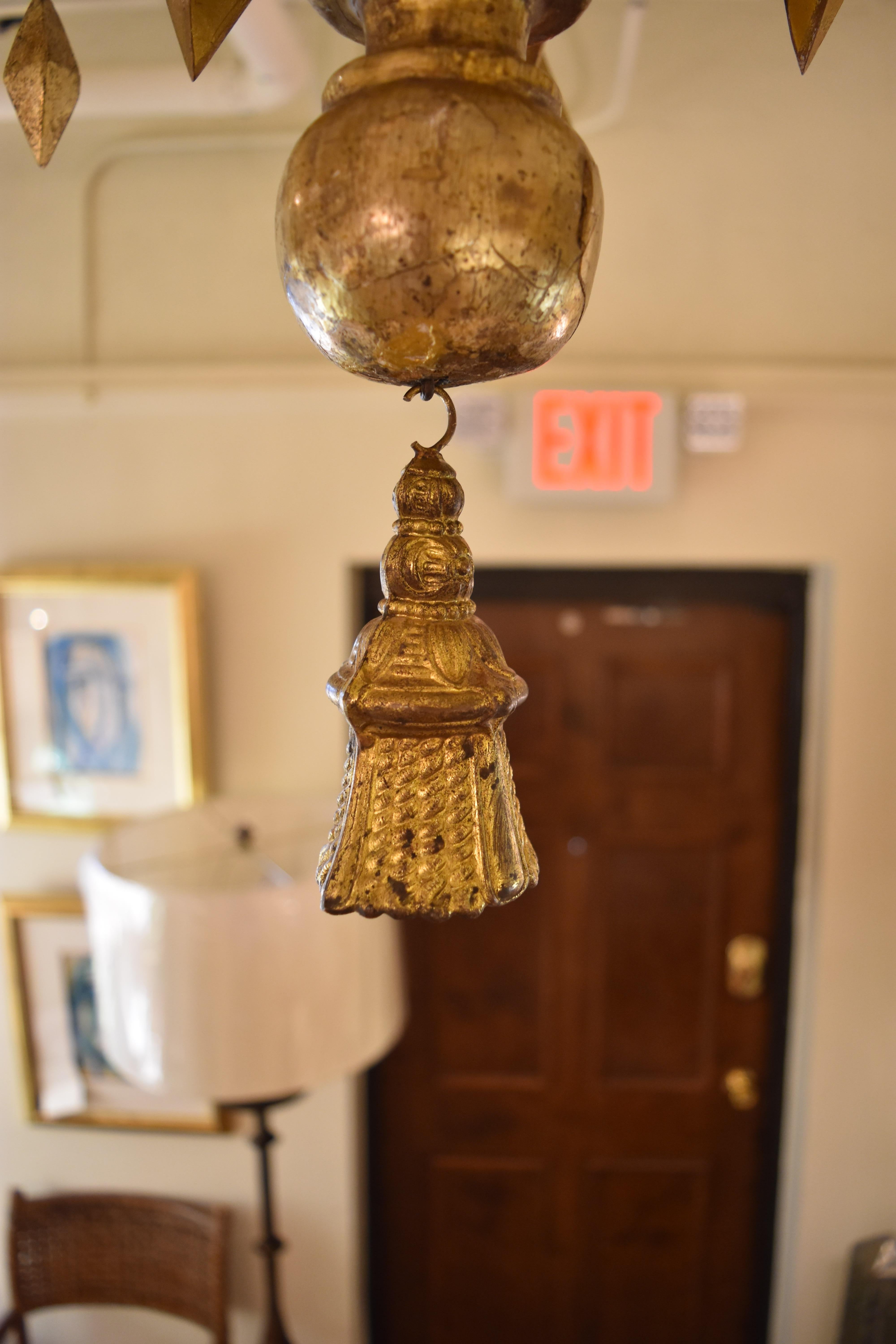 This unique 19th century Italian giltwood chandelier features a transitional geometric design with five scrolling arms with diamond shaped prisms embellishing each arm. The finish is a bright gold with some minor chipping. There is also a decorative