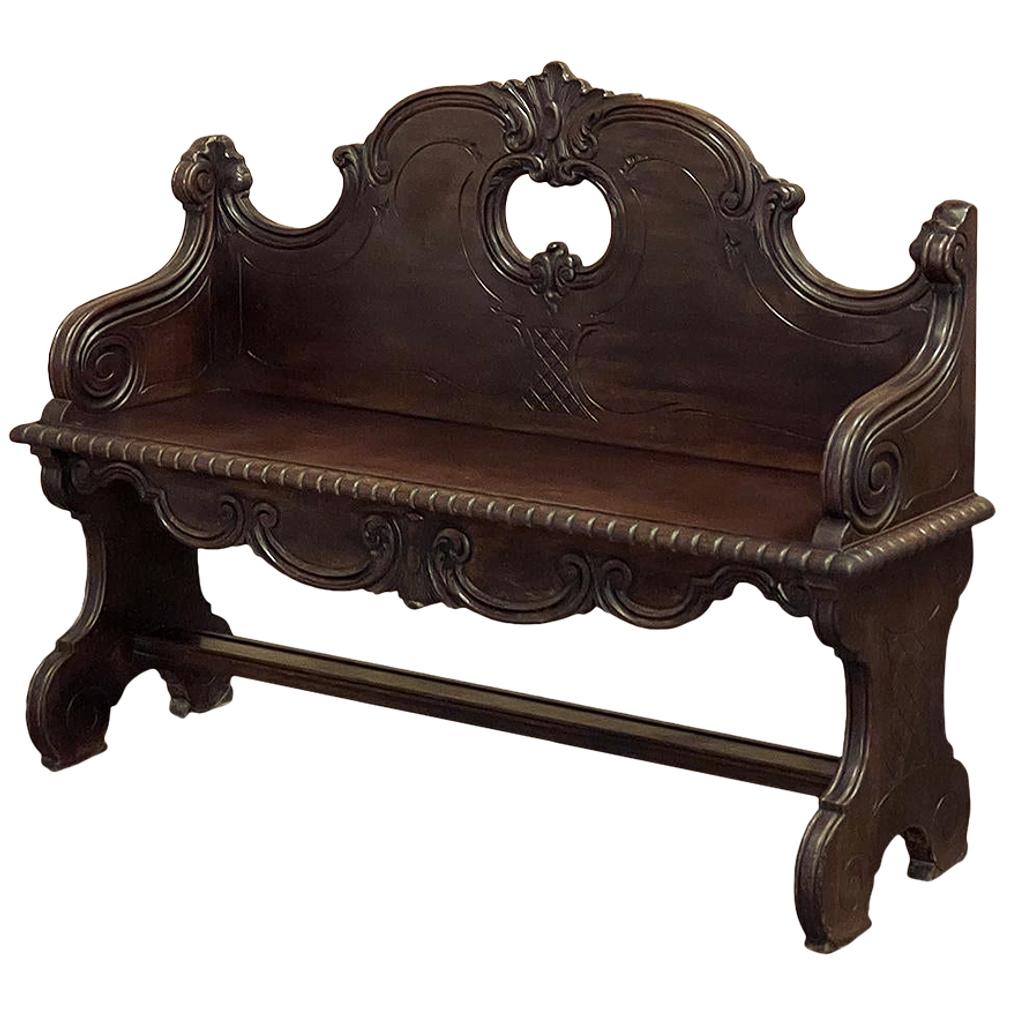 19th Century Italian hall bench was sculpted from fine walnut, and features an elaborately scrolled design including a boldly arched seatback embellished with foliate scrollwork and centered with a stylized shell shield motif appearing over an